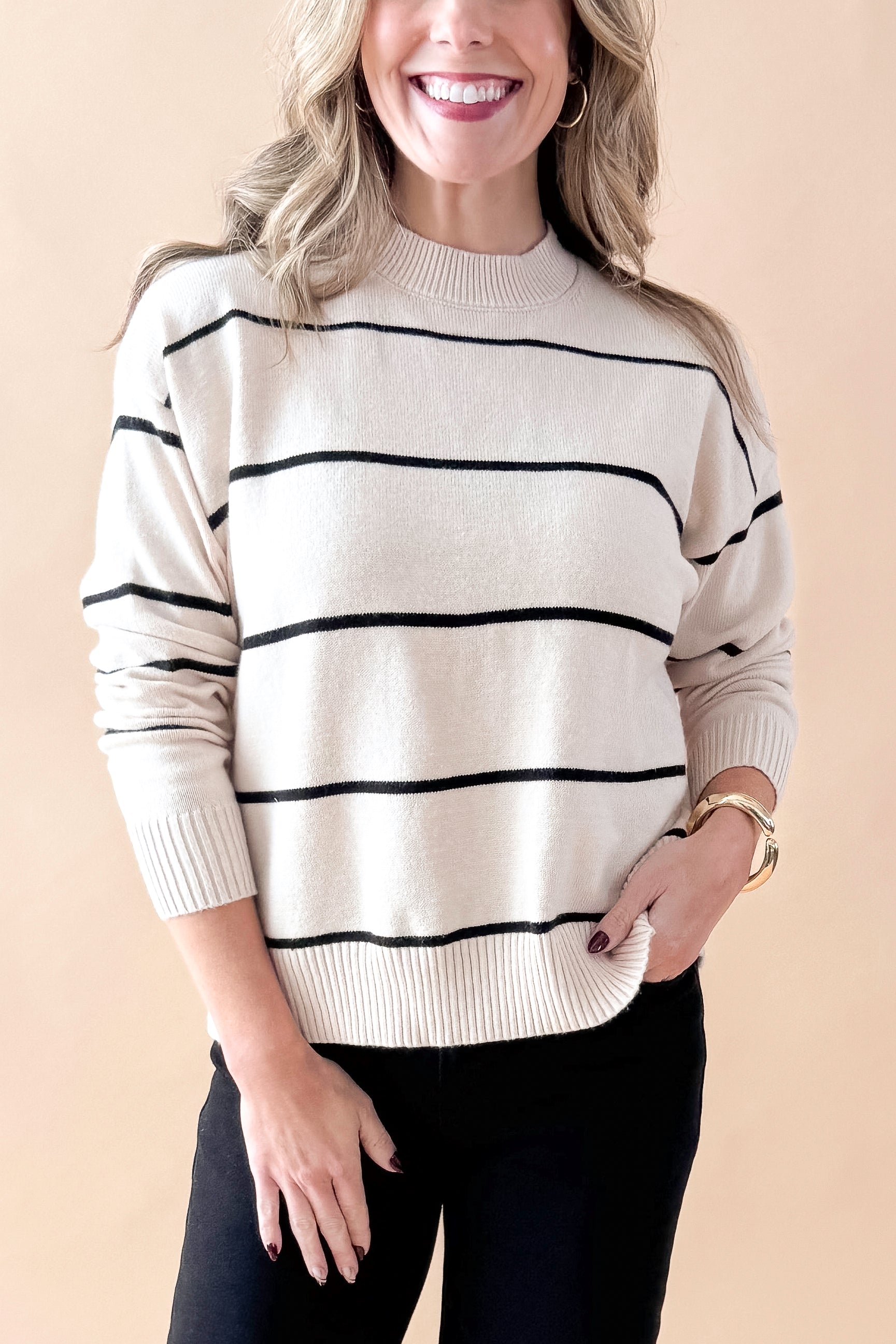 Front detailed view of woman wearing striped sweater with jeans against tan studio background.