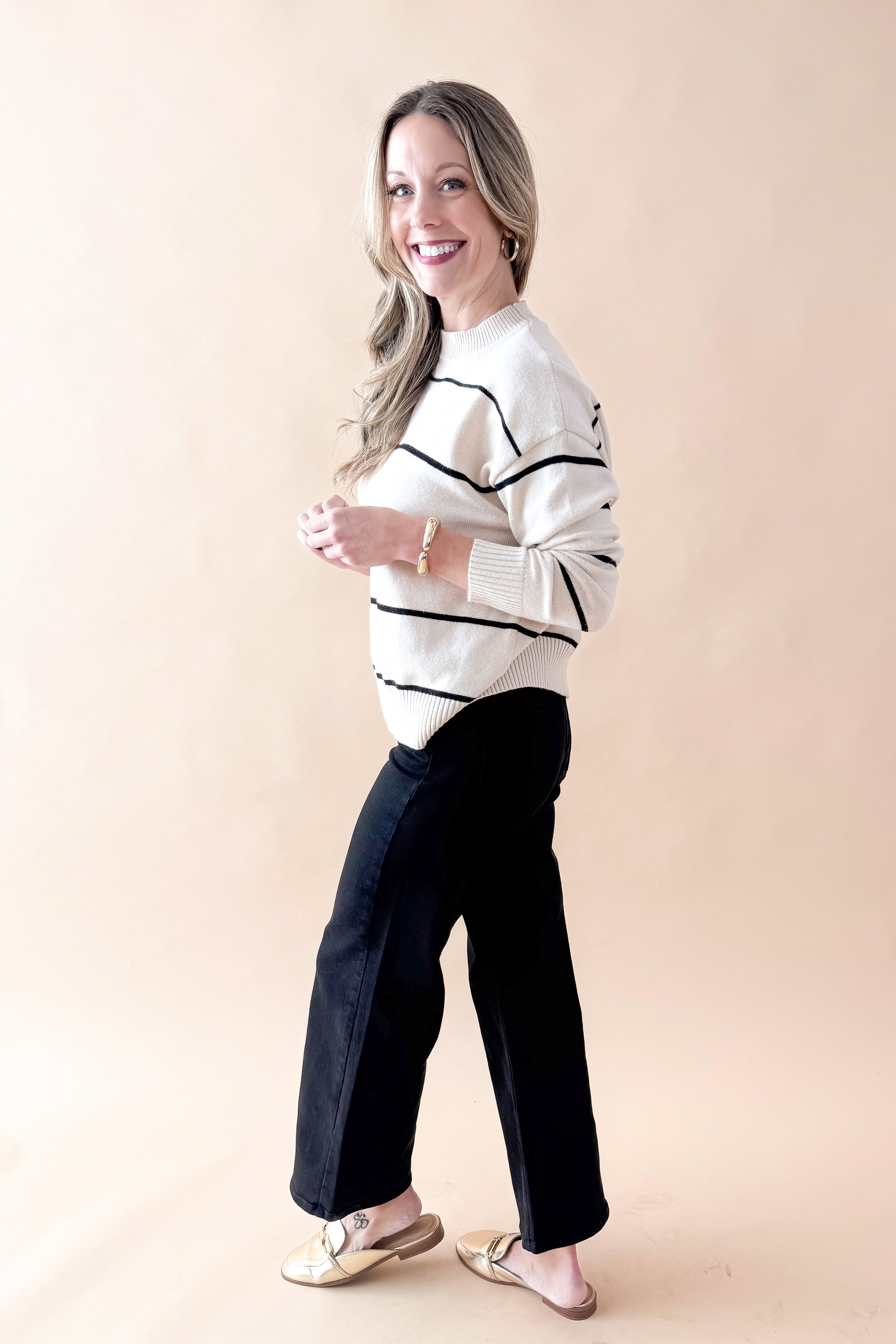 Side view of woman wearing striped sweater with jeans against tan studio background.