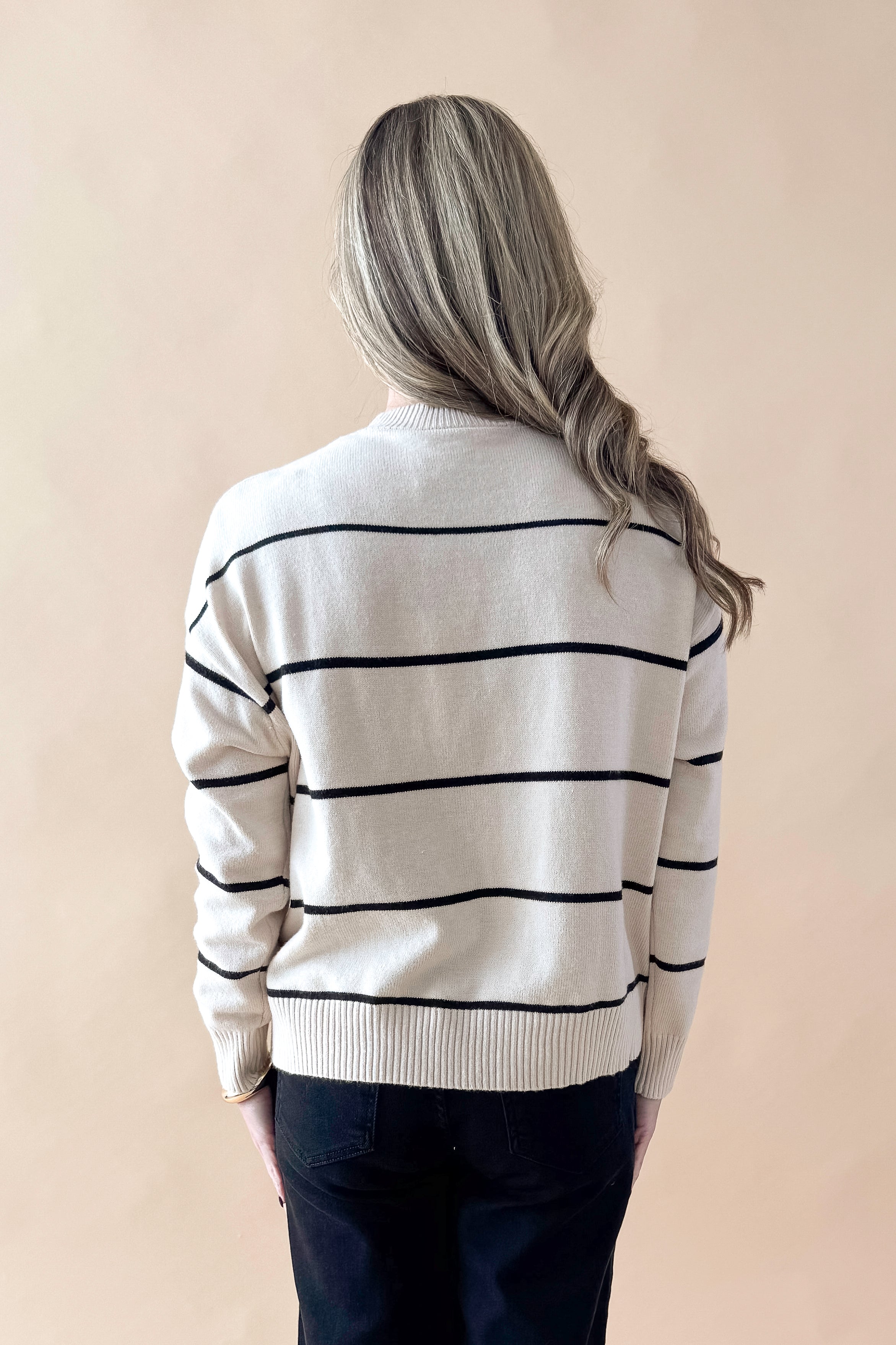 Back view of woman wearing striped sweater with jeans against tan studio background.