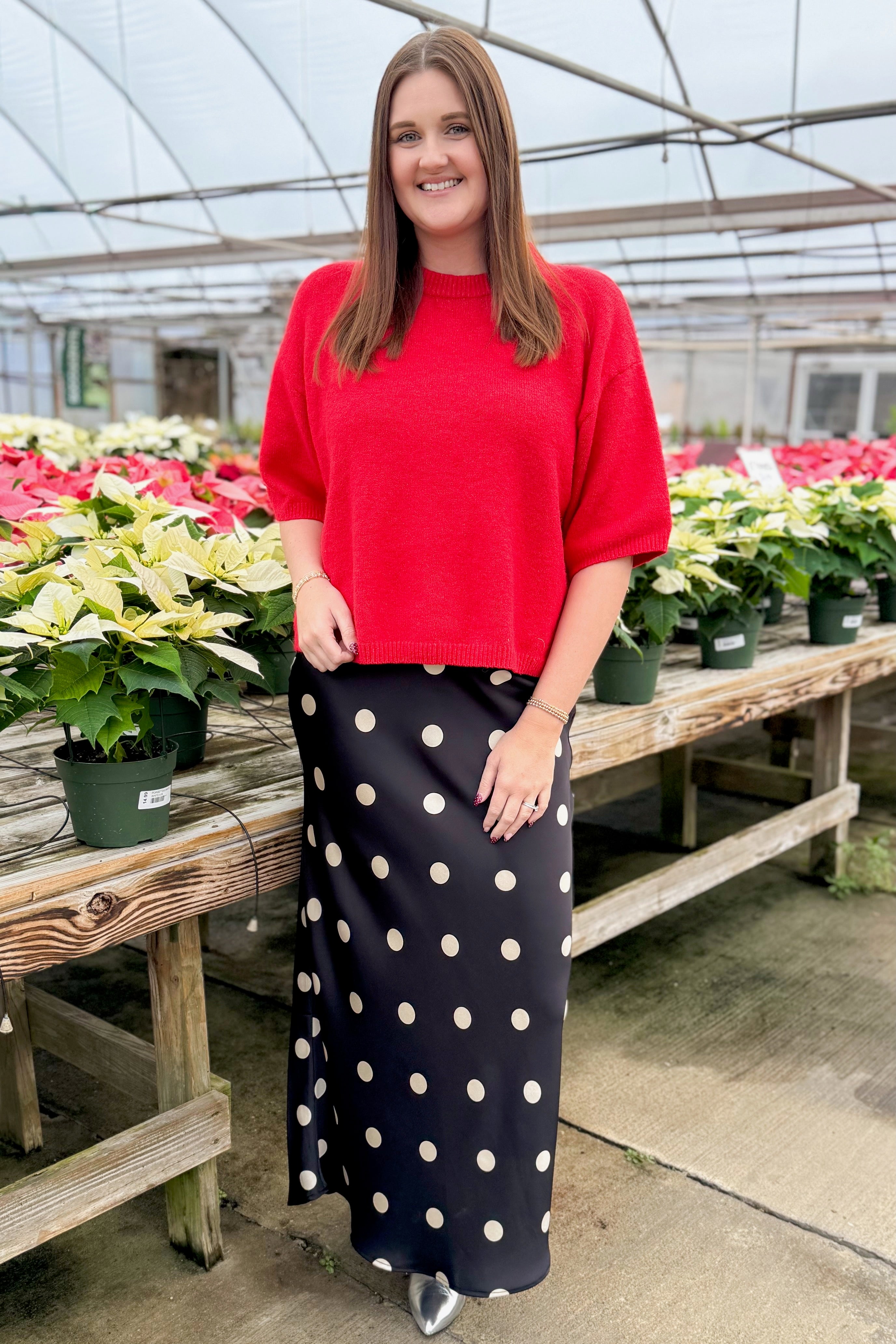 Person wearing a red sweater and skirt with poinsettias in the background.
