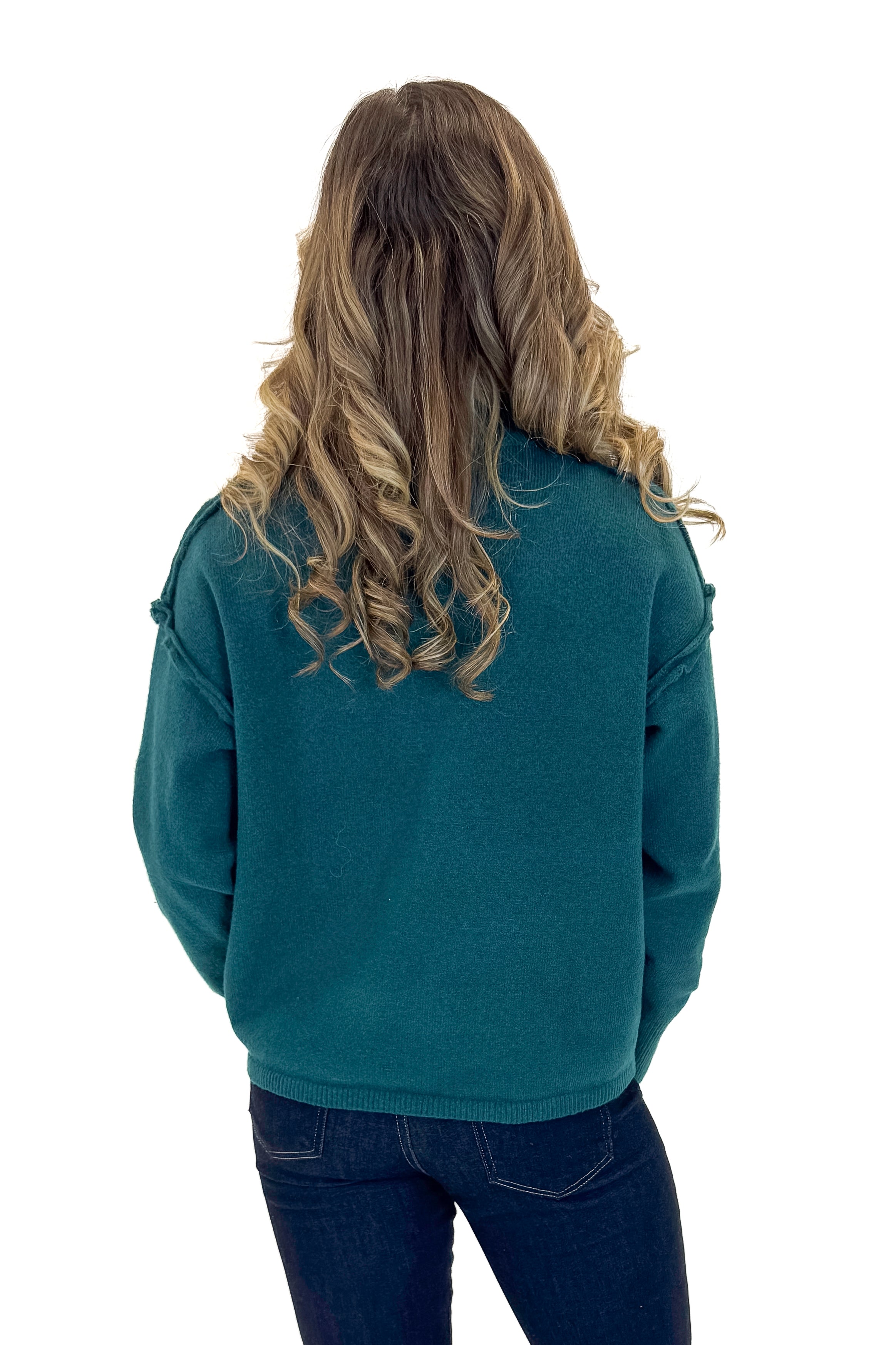 Back view of woman wearing Green Mock Neck Sweater with jeans against white studio background.