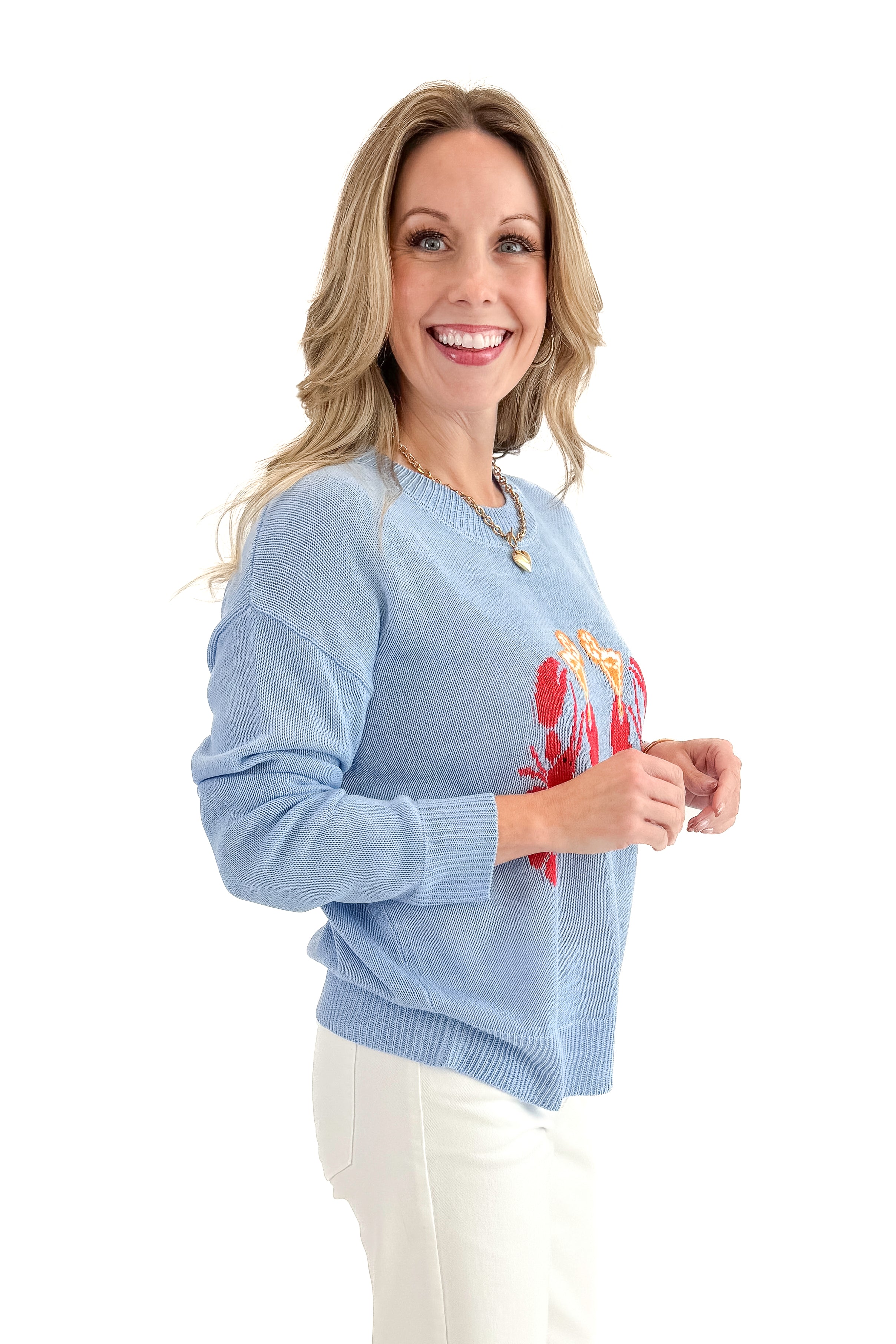 Side view of woman wearing Blue Lobster Graphic Sweater with jeans against white studio background.