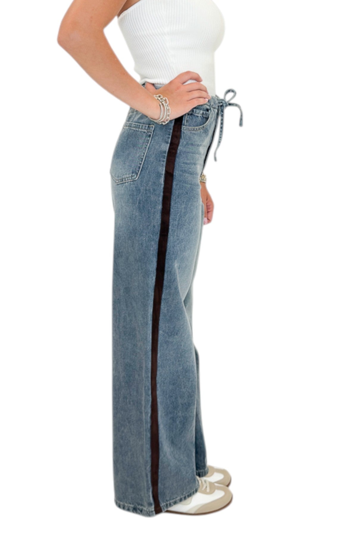 Side view of woman wearing Swagger Boutiqueβs Medium Wash Brown Stripe Detail Jeans against white studio background.