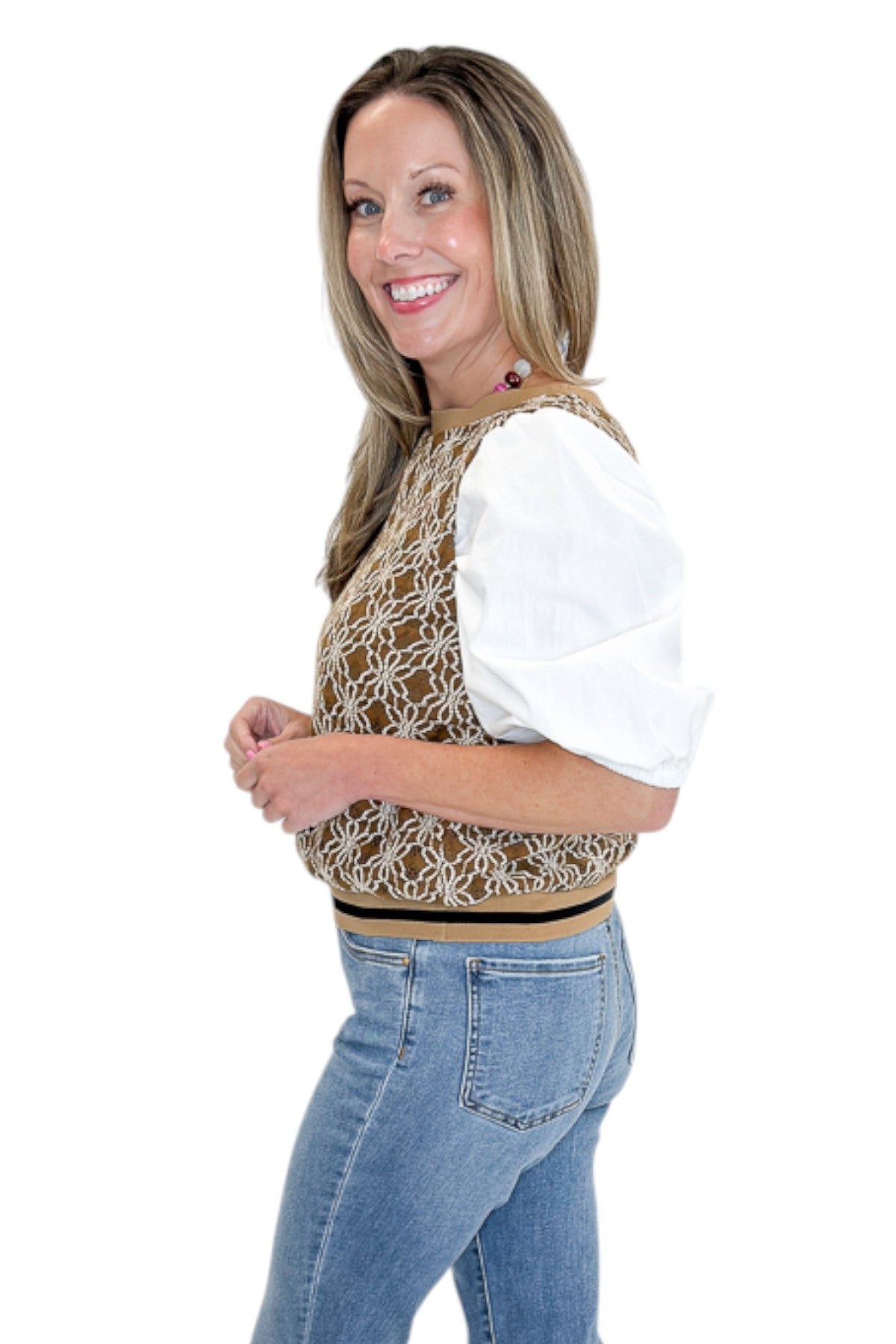 Side view of woman wearing Swagger Boutiqueās Mocha Floral Crocheted Contrast Sleeve Top with jeans against white studio background.