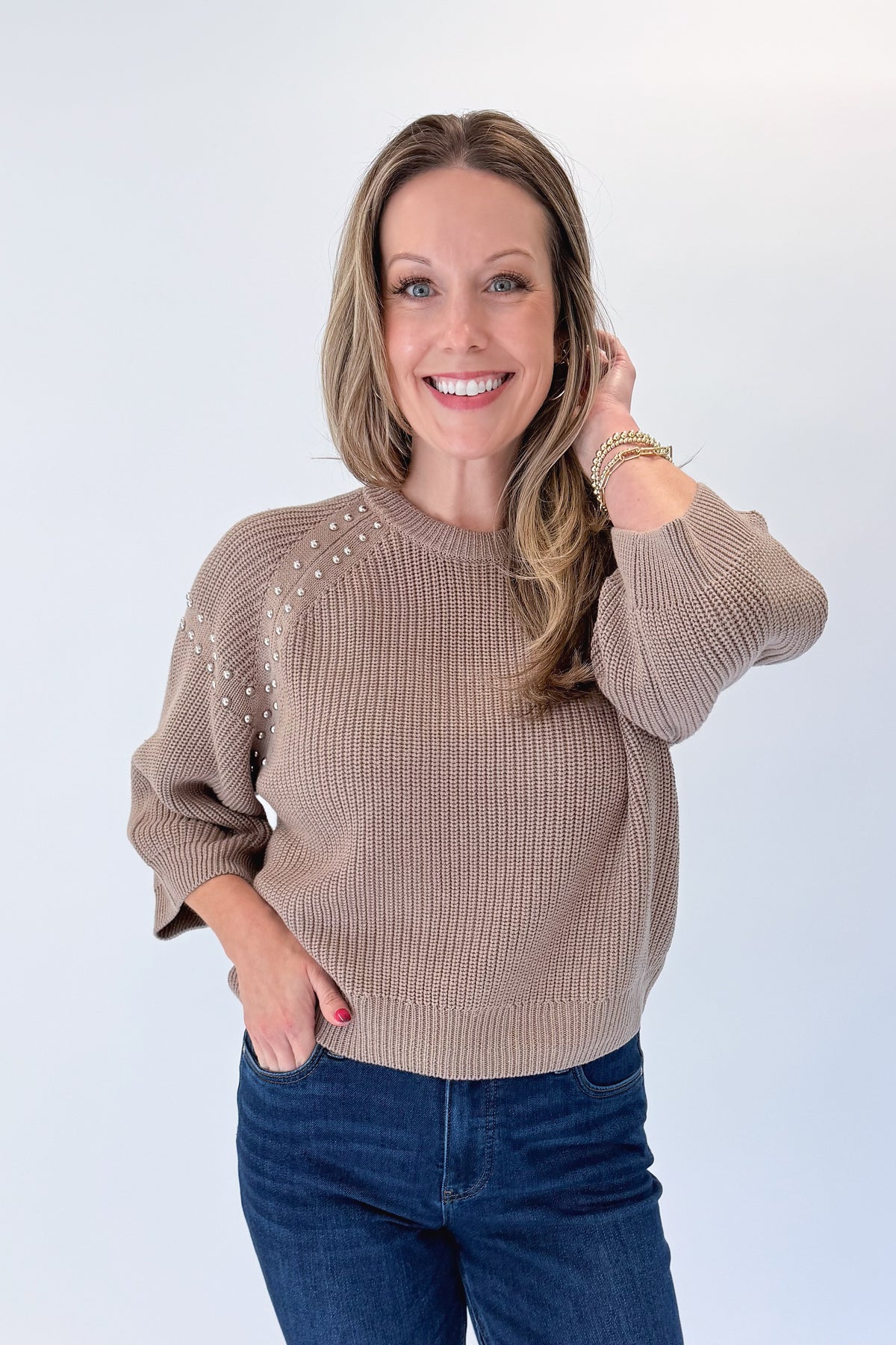 Front view of woman wearing Swagger Boutique’s Mocha Stud Detail Sweater by Entro with jeans against white studio background.