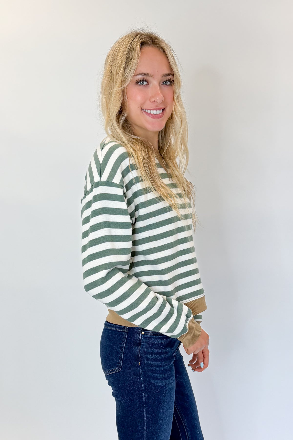 Side view of woman wearing Swagger Boutique’s Monstera Low Key Stripe Sweatshirt by Z Supply with jeans against white studio background.