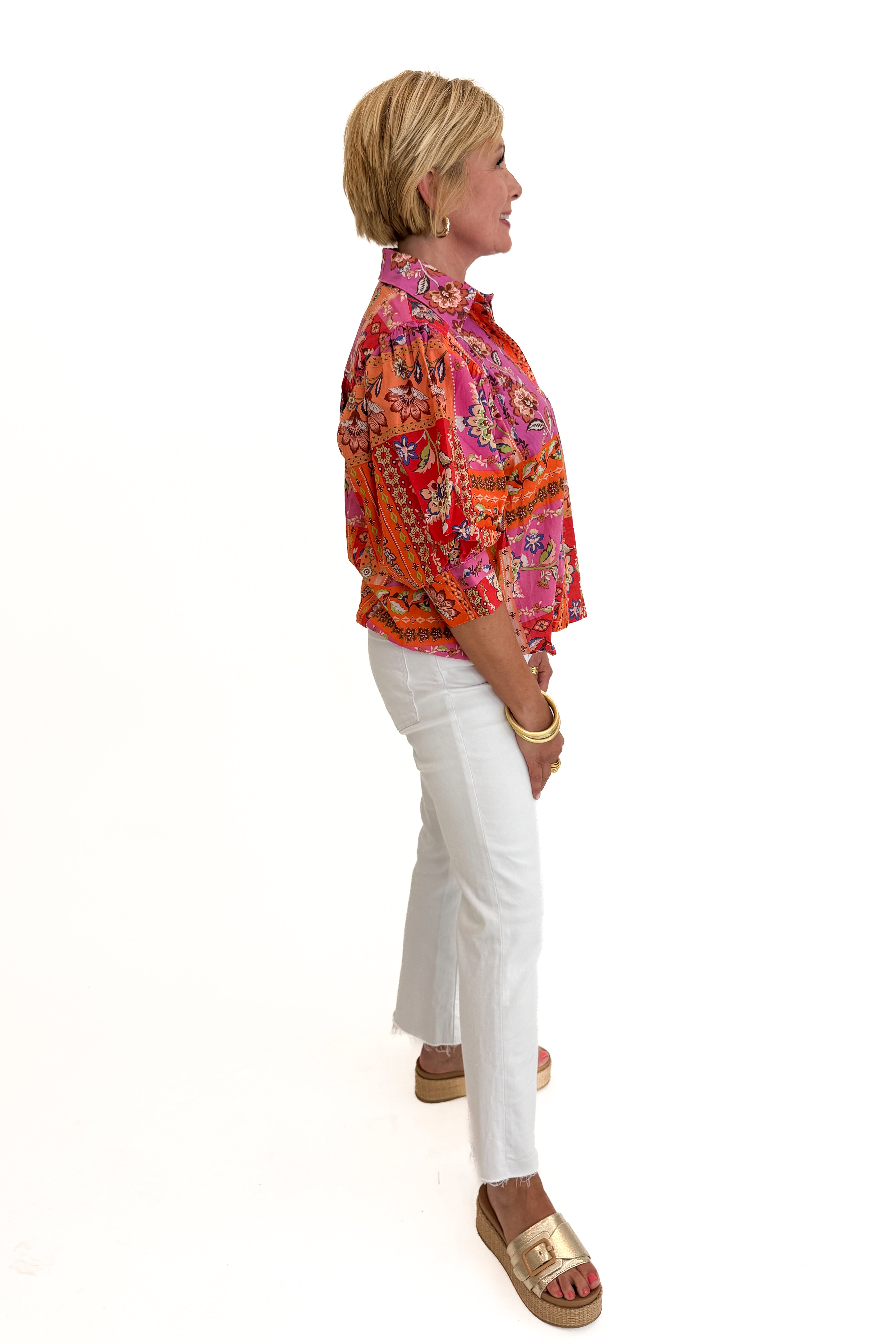 Side view of woman wearing Swagger Boutiqueโs Multi Floral Patchwork Top with jeans against white studio background.