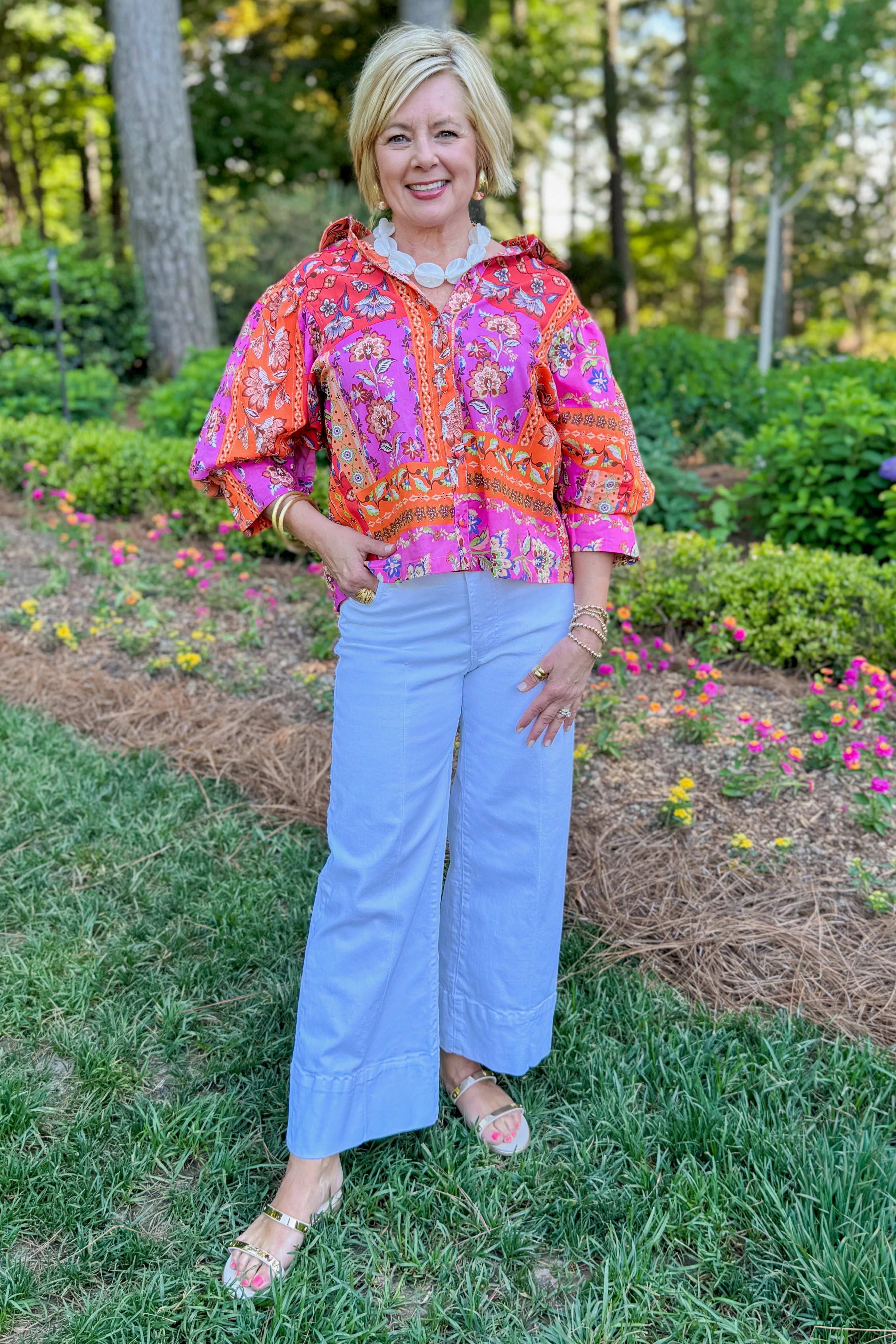 Front view of woman wearing Swagger Boutiqueโs Multi Floral Patchwork Top with jeans standing outside.