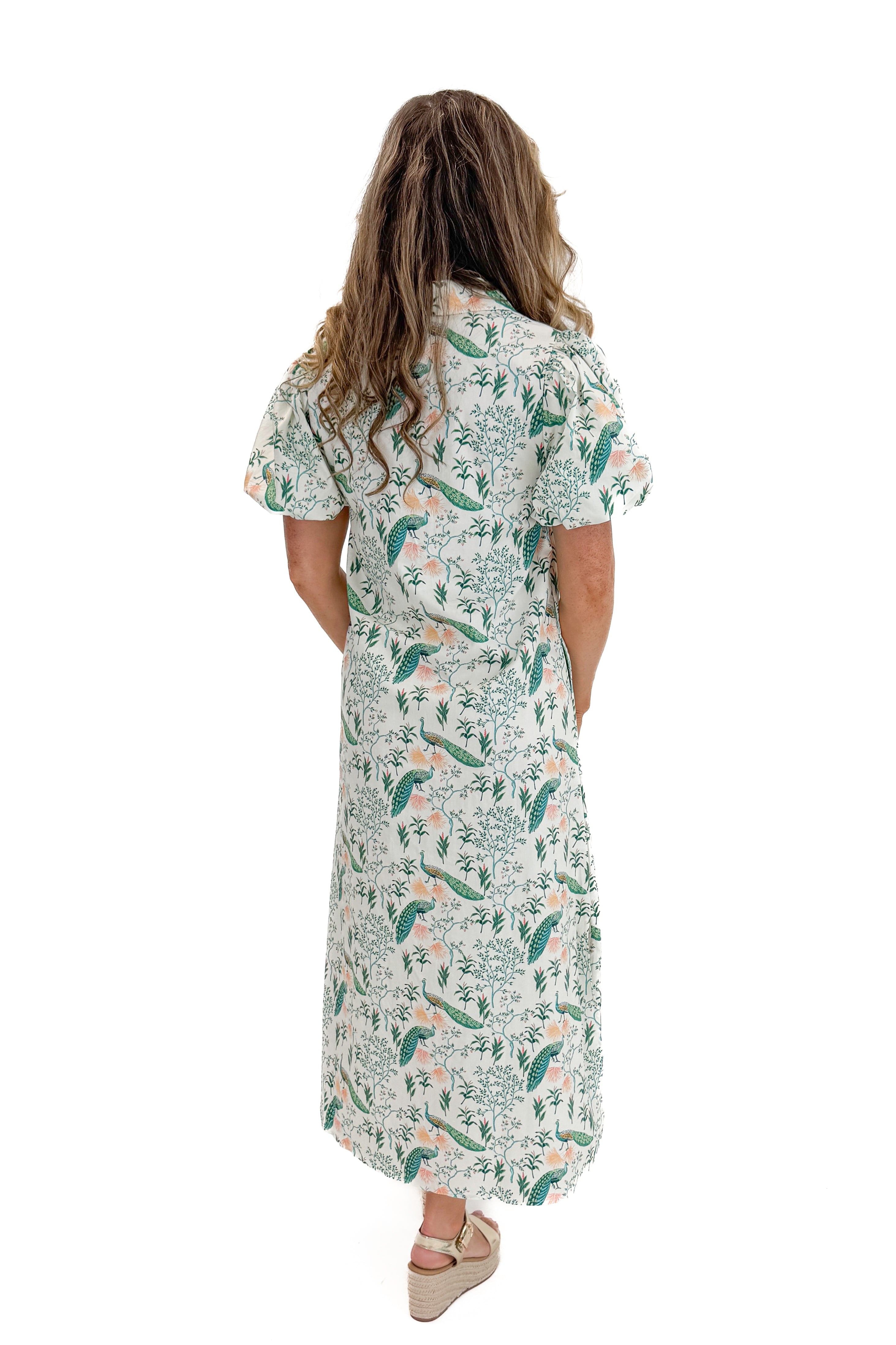 Back view of woman wearing Swagger Boutiqueβs Multi Peacock Print Maxi Dress with sandals against white studio background.