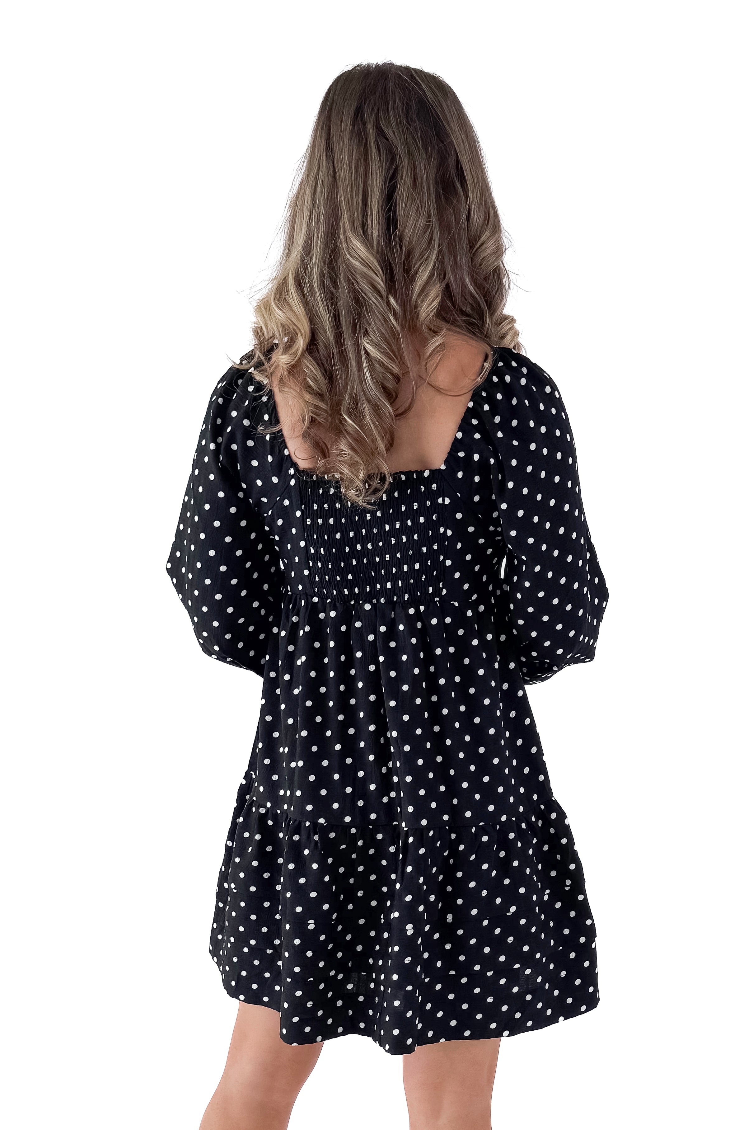 Back view of woman wearing polka dot dress and boots against white studio background.