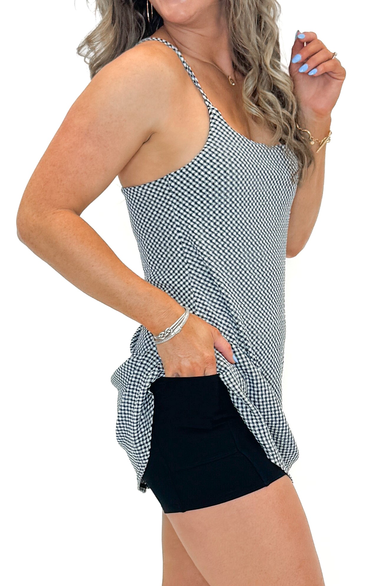 Side detail view of woman wearing Black & White Checkered Tennis Dress with sneakers against white studio background.