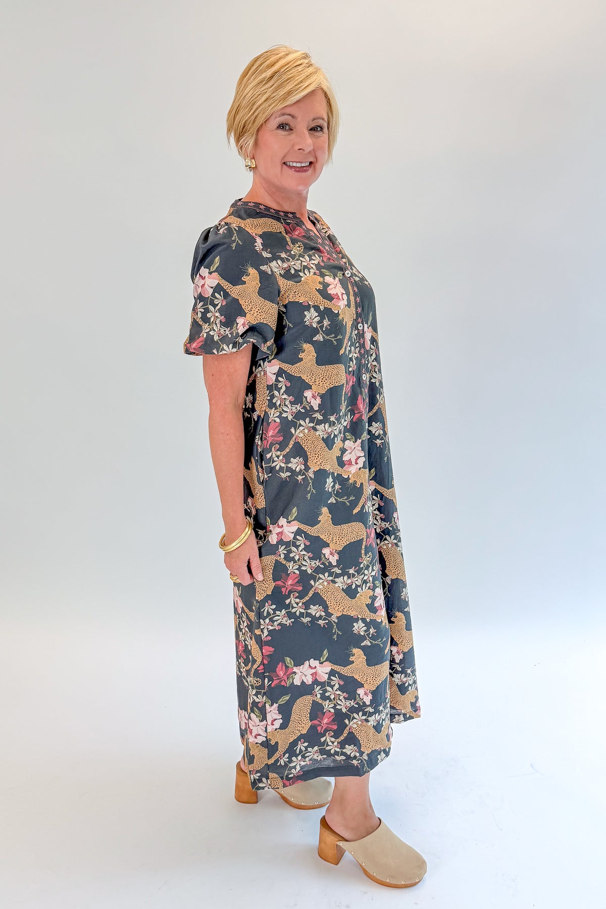 Side view of woman wearing Swagger Boutique’s Navy Animal Print Midi Dress with clogs against white studio background.