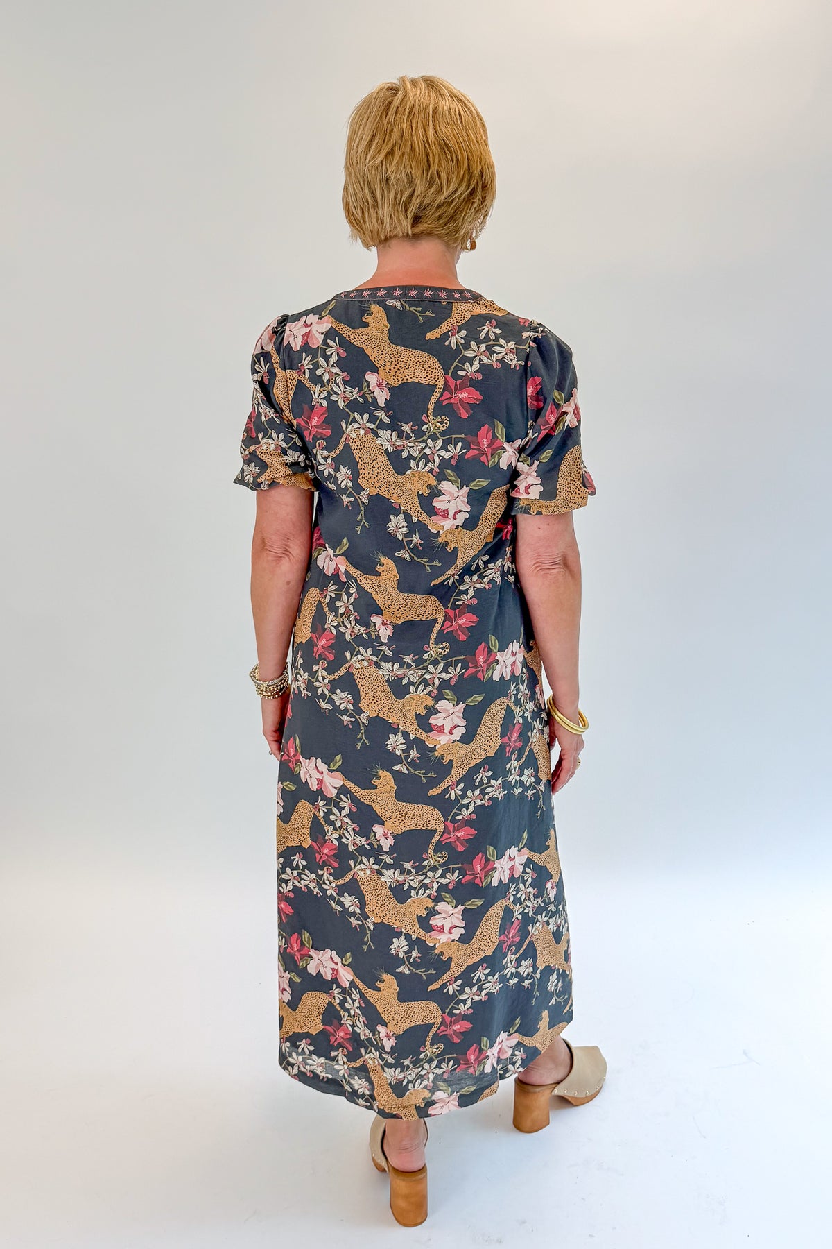 Back view of woman wearing Swagger Boutique’s Navy Animal Print Midi Dress with clogs against white studio background.