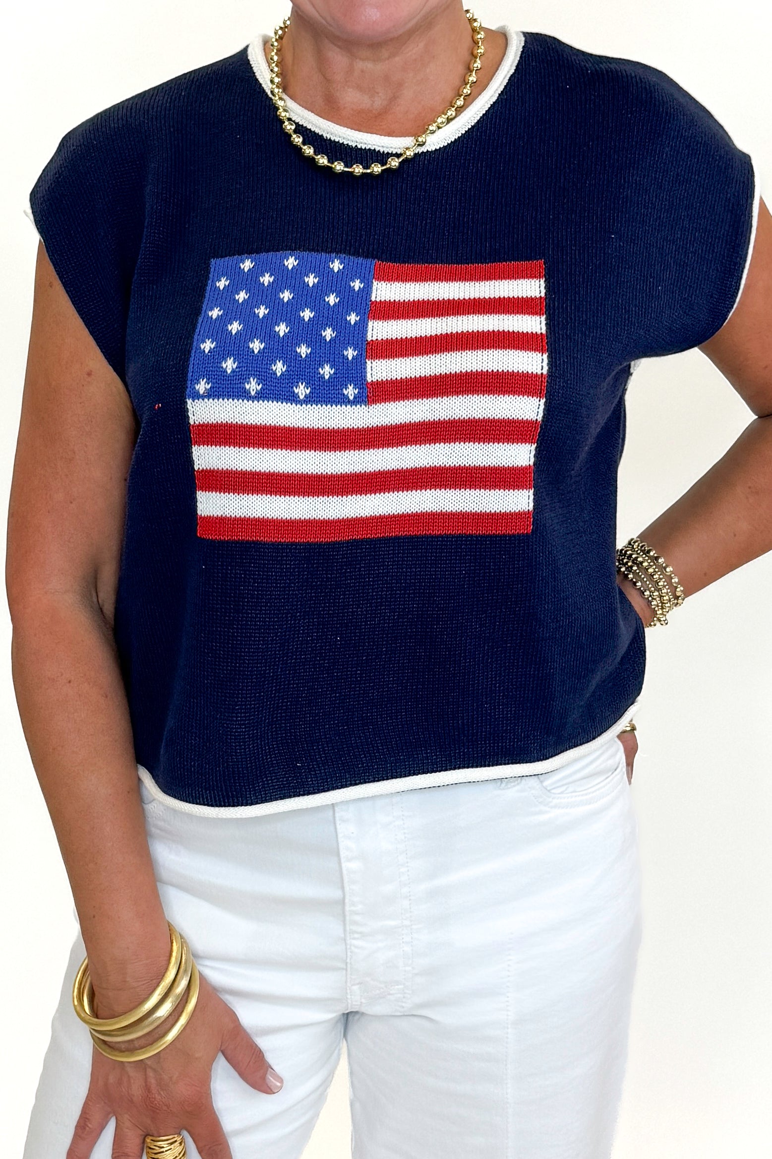 Front detail view of woman wearing Swagger Boutiqueโs Right On Cue Navy Flag Short Sleeve Sweater with jeans against white studio background.