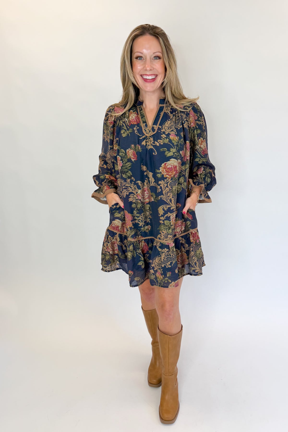 Front view of woman wearing Swagger Boutique’s Navy Floral Print Mini Dress with boots against white studio background.