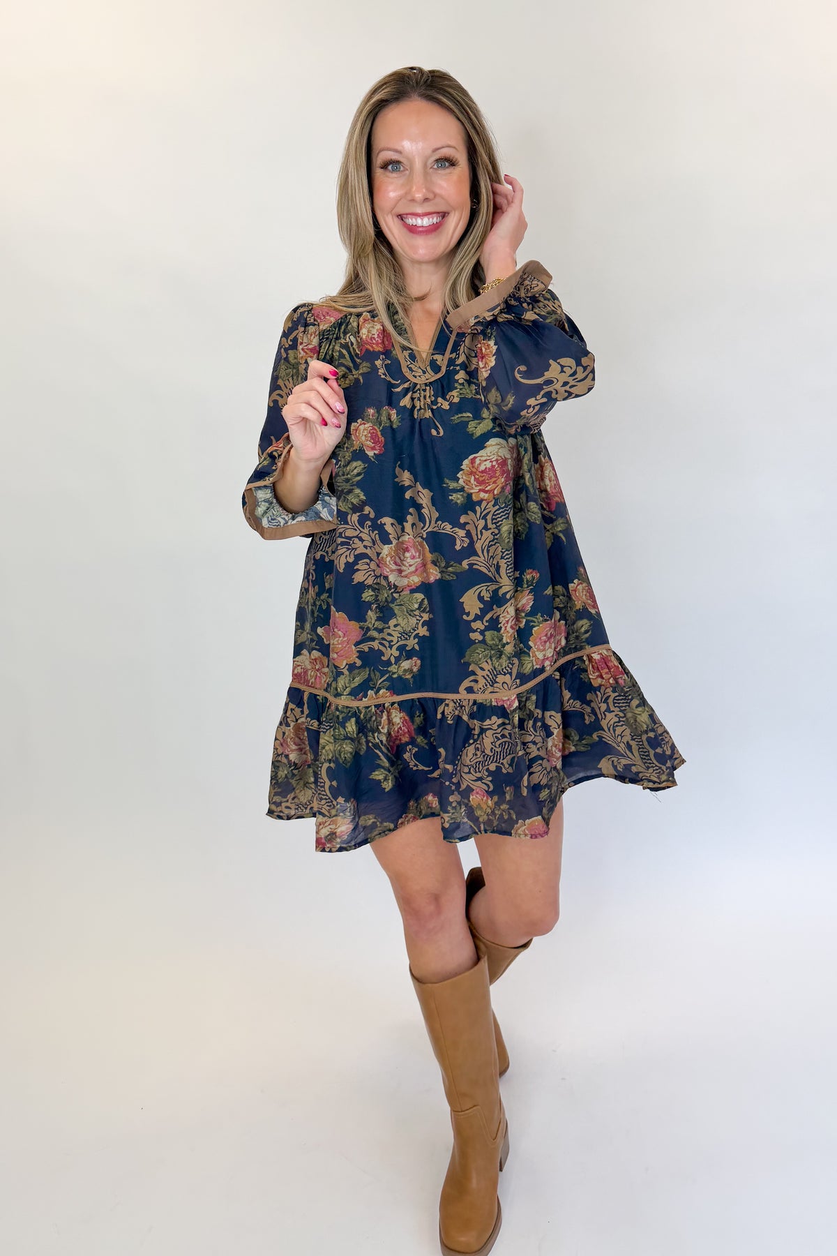 Front view of woman wearing Swagger Boutique’s Navy Floral Print Mini Dress with boots against white studio background.