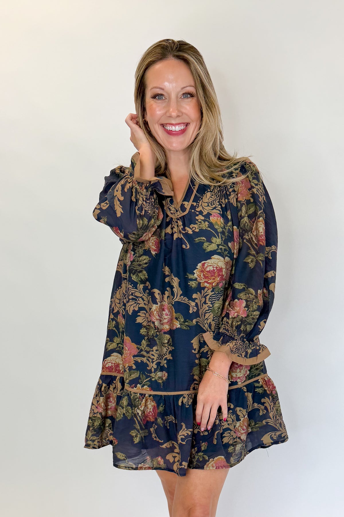 Front view of woman wearing Swagger Boutique’s Navy Floral Print Mini Dress with boots against white studio background.