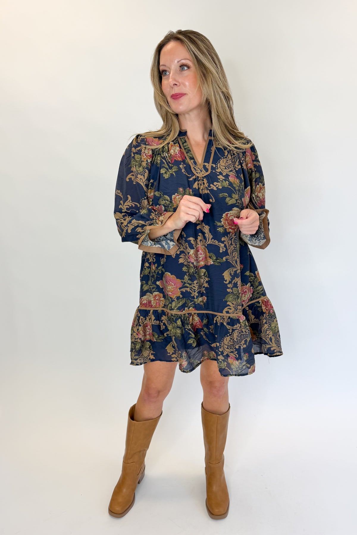 Front view of woman wearing Swagger Boutique’s Navy Floral Print Mini Dress with boots against white studio background.