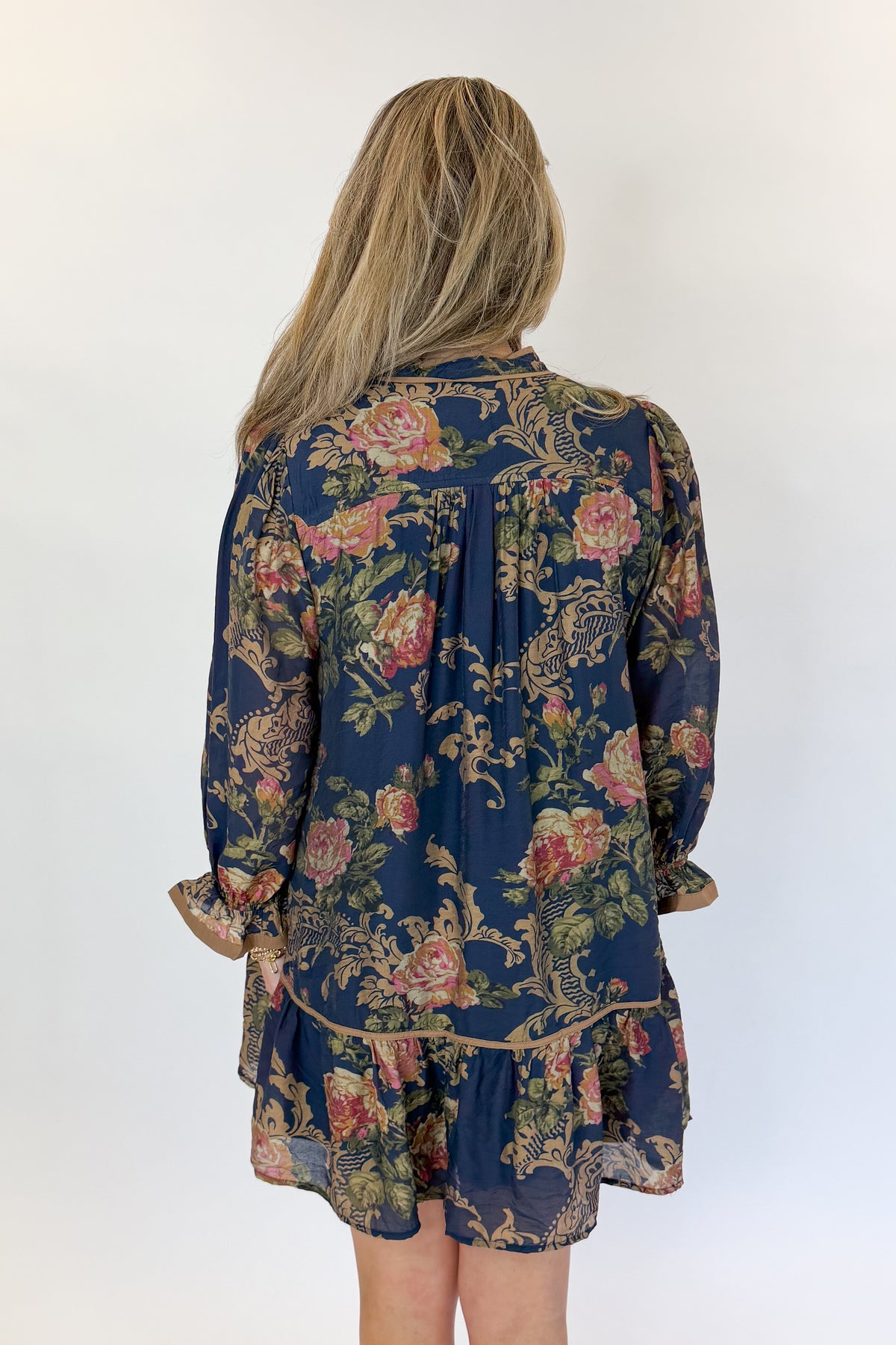 Back view of woman wearing Swagger Boutique’s Navy Floral Print Mini Dress with boots against white studio background.