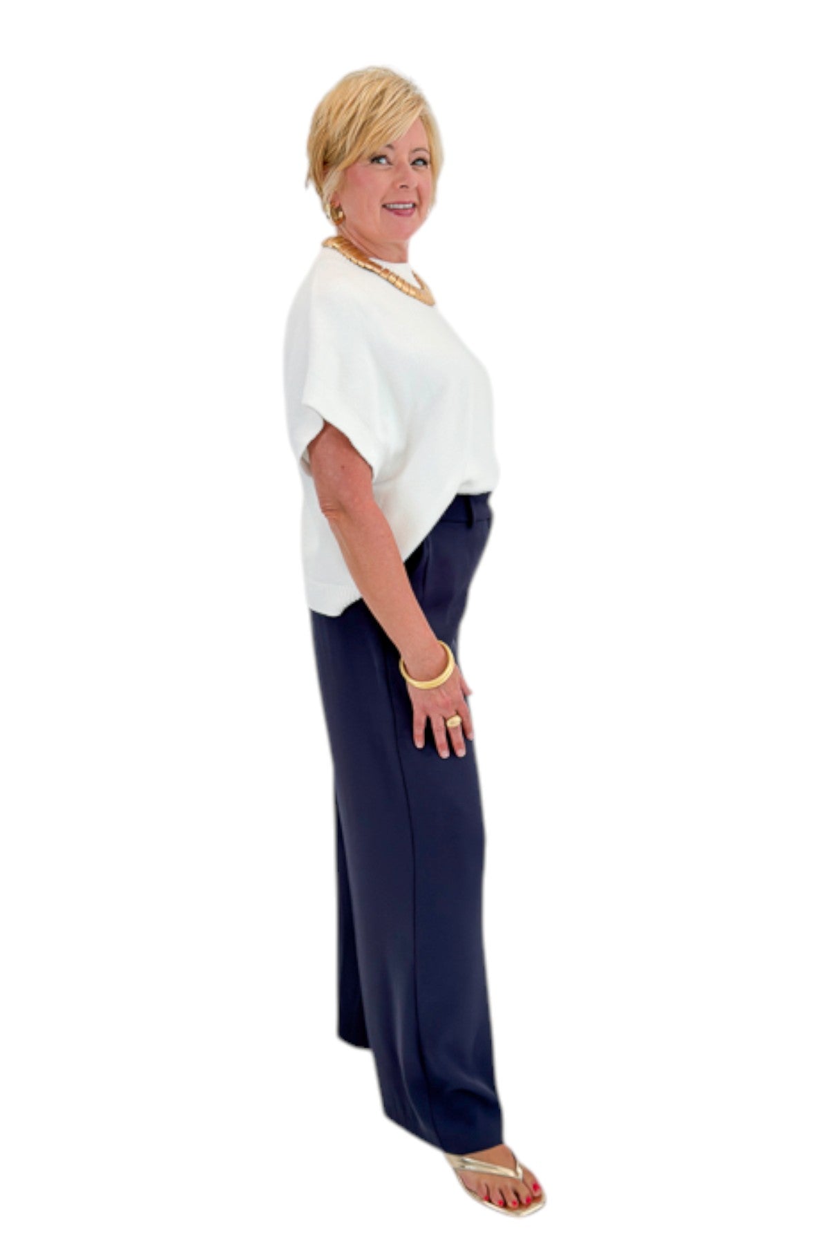 Side view of woman wearing Swagger Boutiqueās Ivory Light Weight Short Sleeve Sweater with Navy High Waisted Trousers by Skies Are Blue against white studio background.