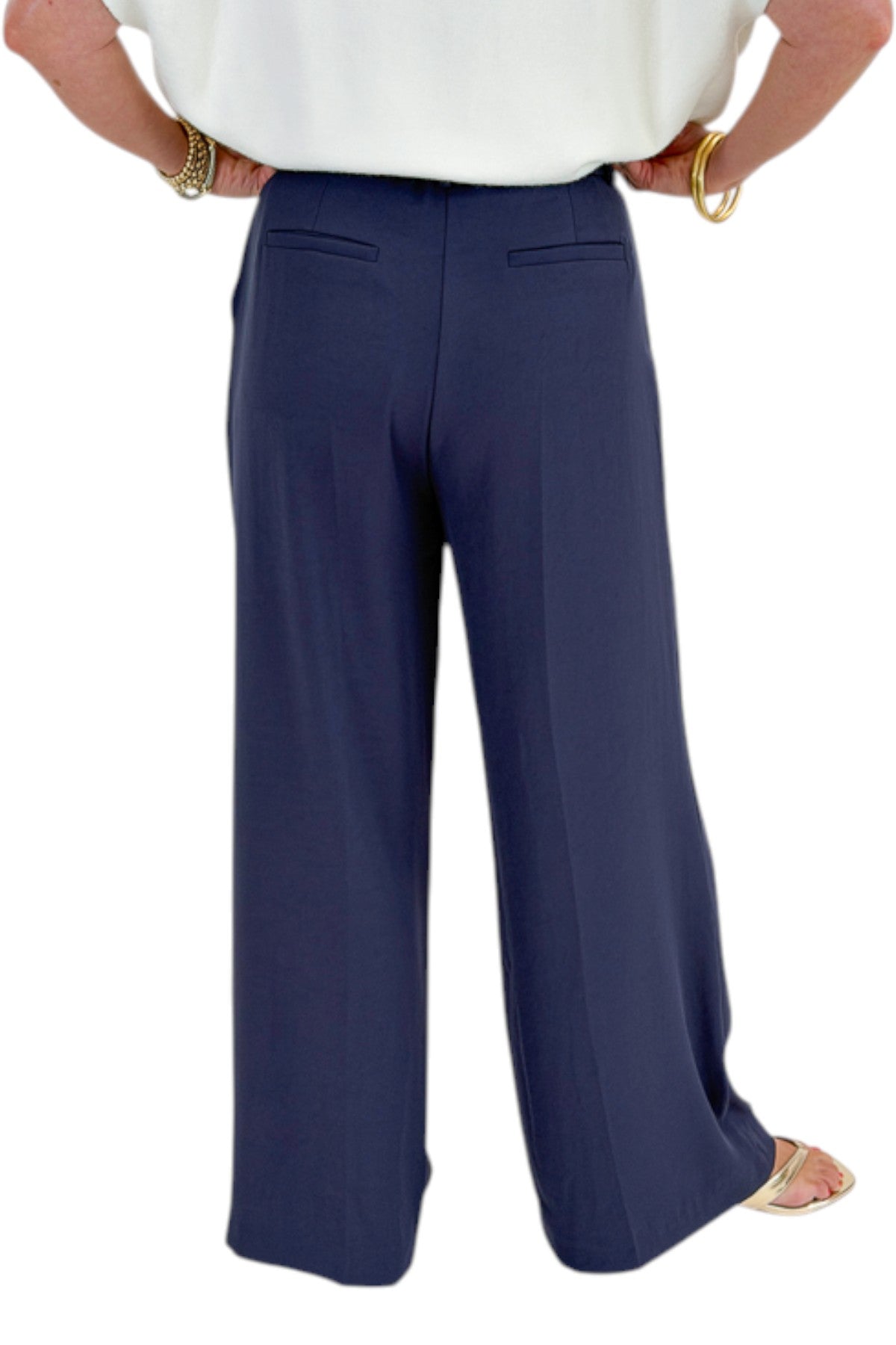 Back detail view of woman wearing Swagger Boutiqueās Ivory Light Weight Short Sleeve Sweater with Navy High Waisted Trousers by Skies Are Blue against white studio background.