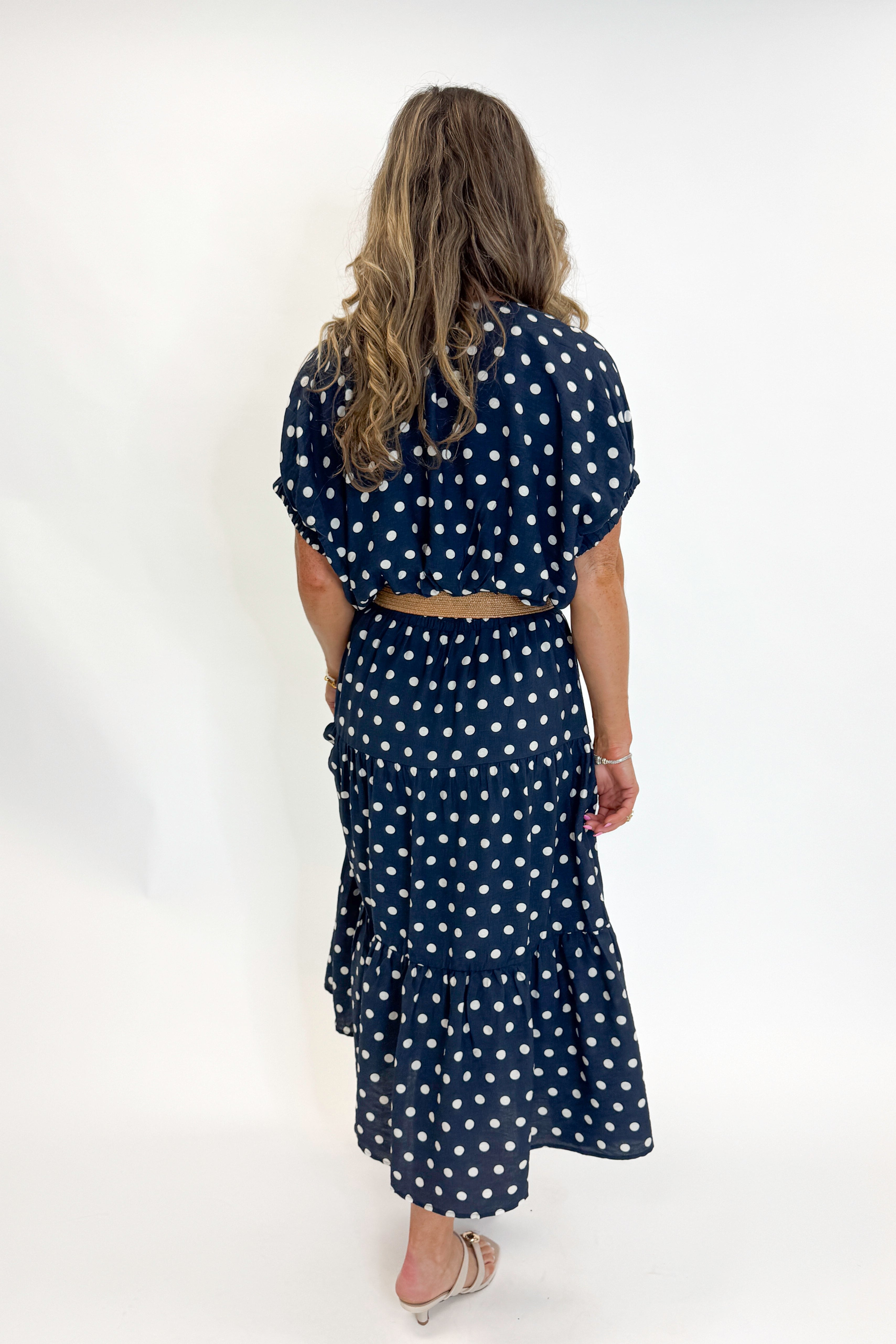 Back view of woman wearing Swagger Boutiqueβs Navy Polka Dot Bubble Hem Top by Entro with matching Navy Polka Dot Tiered Skirt by Entro against white studio background.