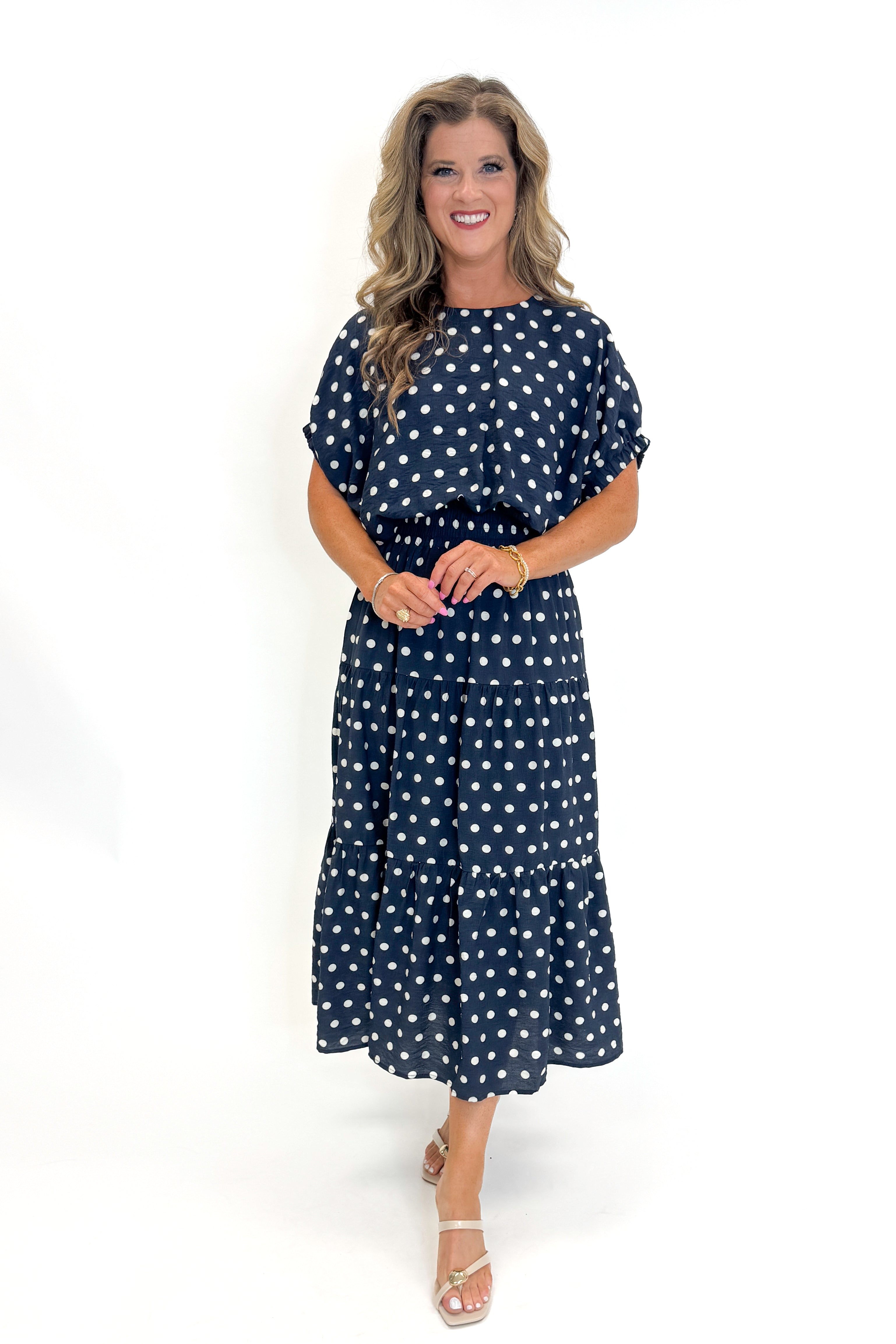 Front view of woman wearing Swagger Boutiqueβs Navy Polka Dot Bubble Hem Top by Entro with matching Navy Polka Dot Tiered Skirt by Entro against white studio background.