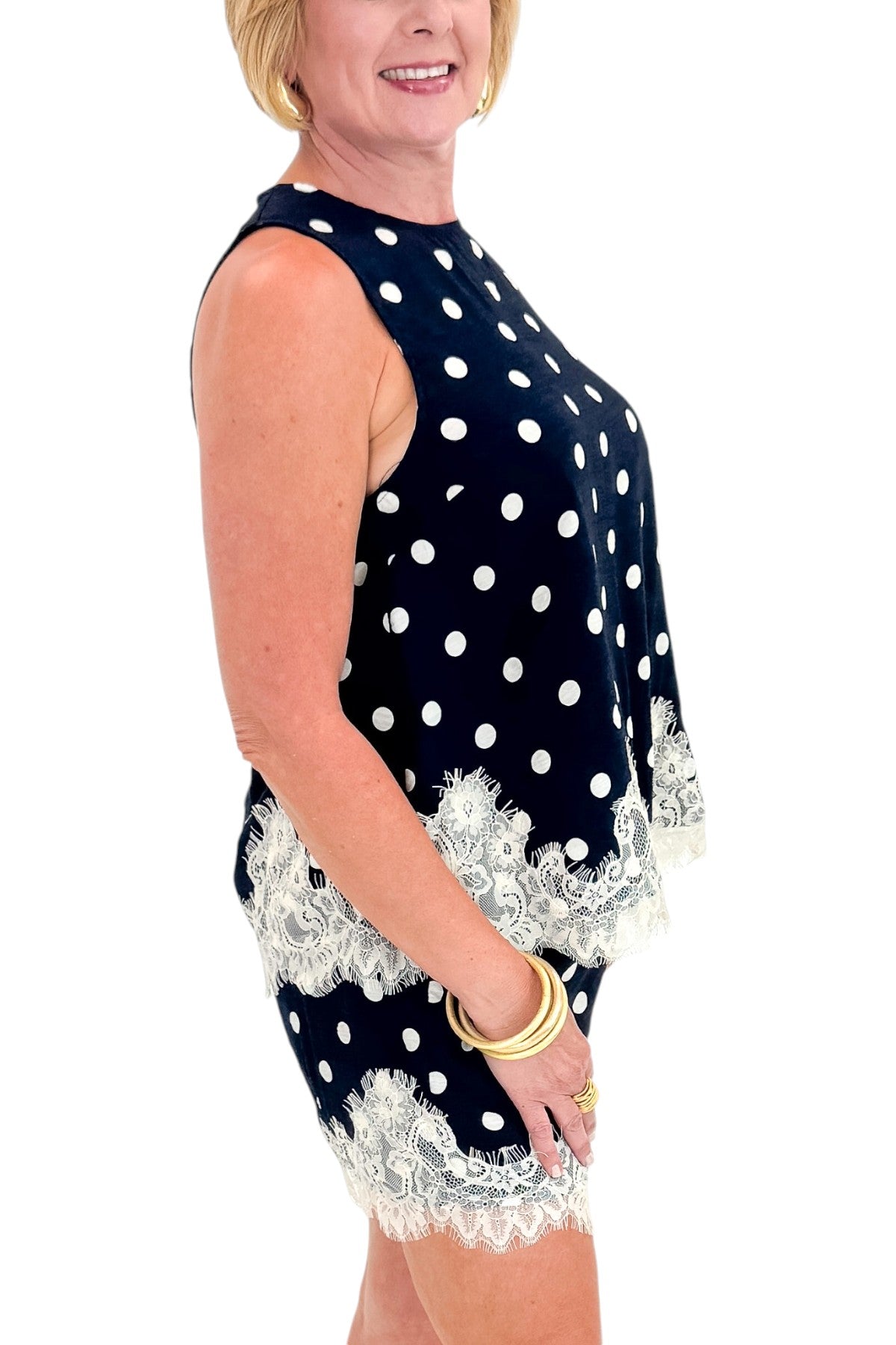 Side detail view of woman wearing Swagger Boutiqueās Navy Polka Dot Lace Trim Shorts by Entro with matching tank against white studio background.