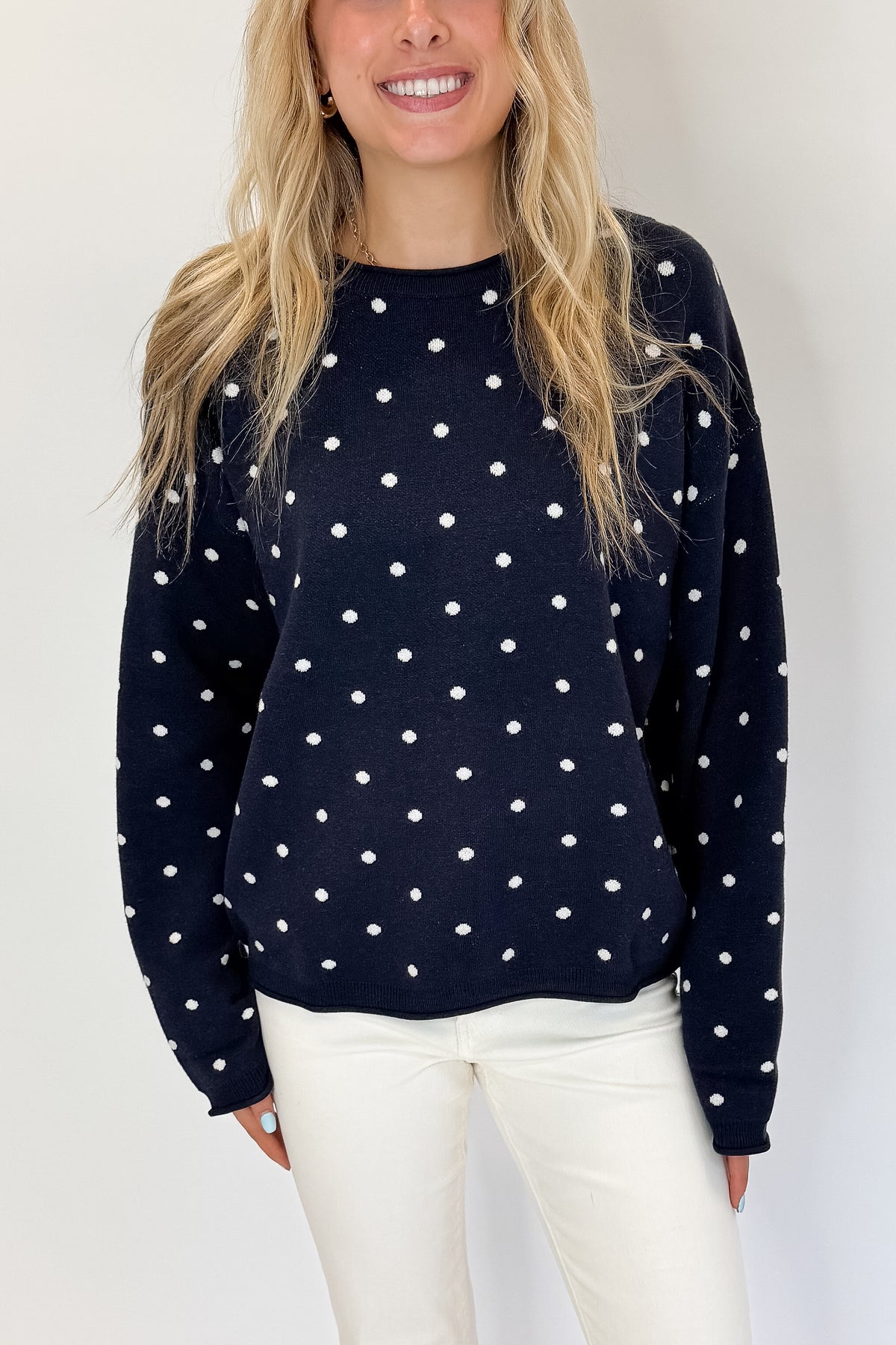 Front detail view of woman wearing Swagger Boutique’s Navy Polka Dot Sweater with jeans against white studio background.