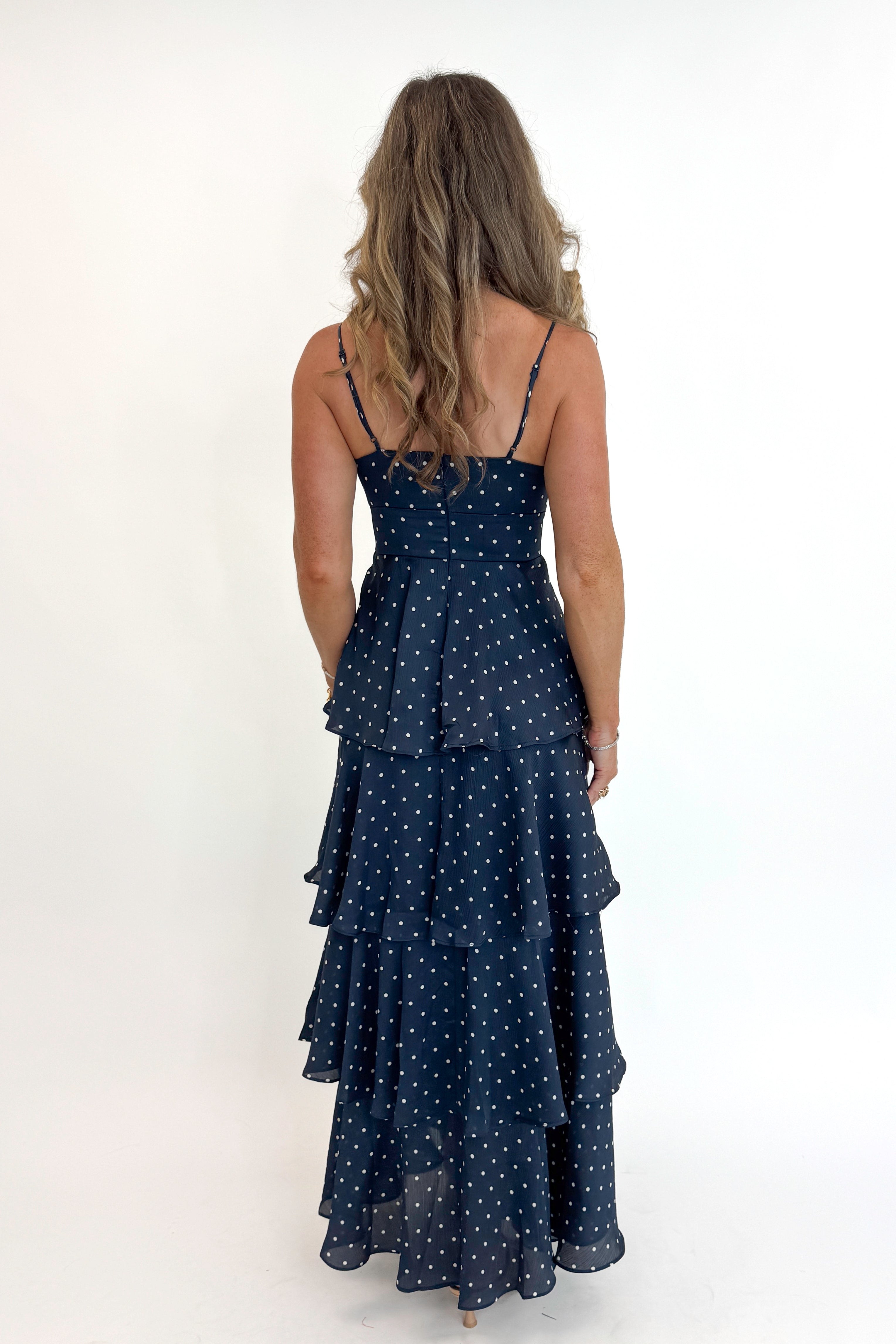 Back view of woman wearing Swagger Boutiqueās Navy Polka Dot Tiered Maxi Dress against white studio background.