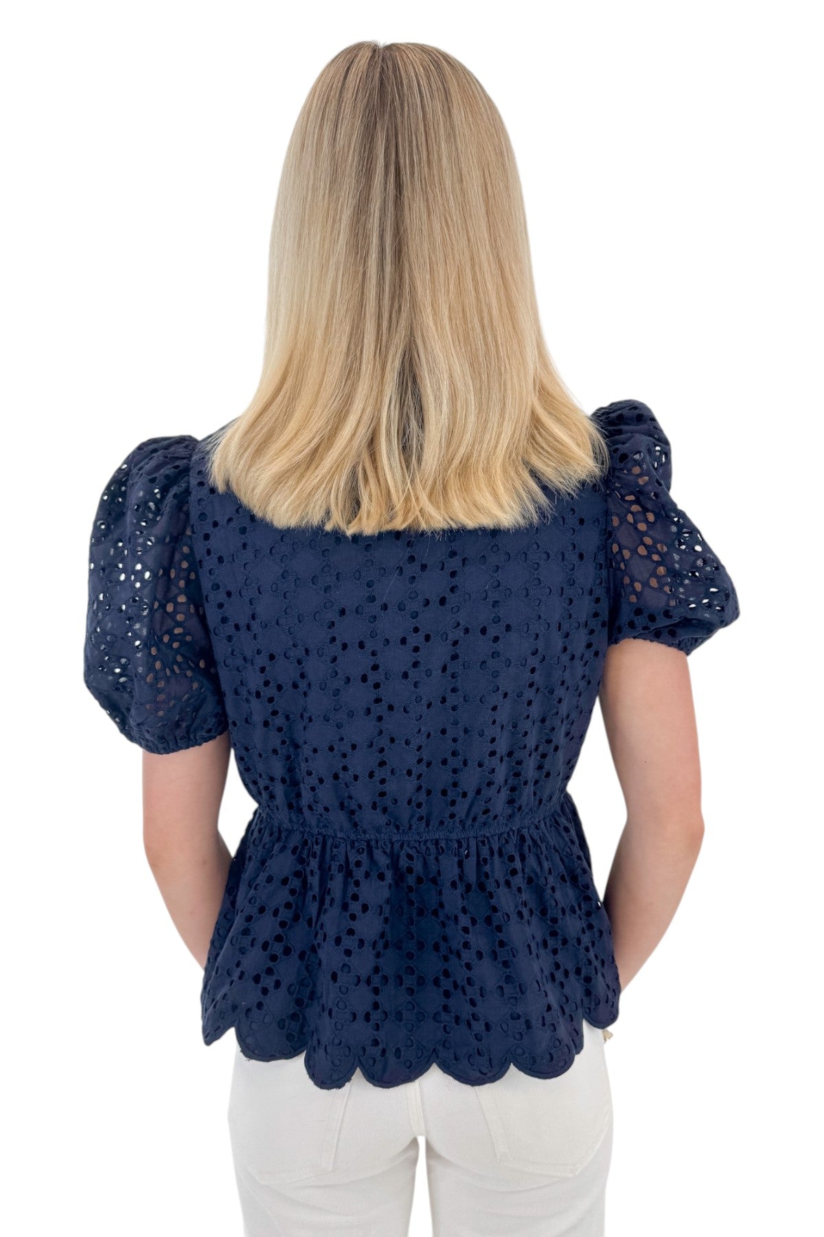 Back view of woman wearing Navy Short Sleeve Peplum Eyelet Top with jeans against white studio background.