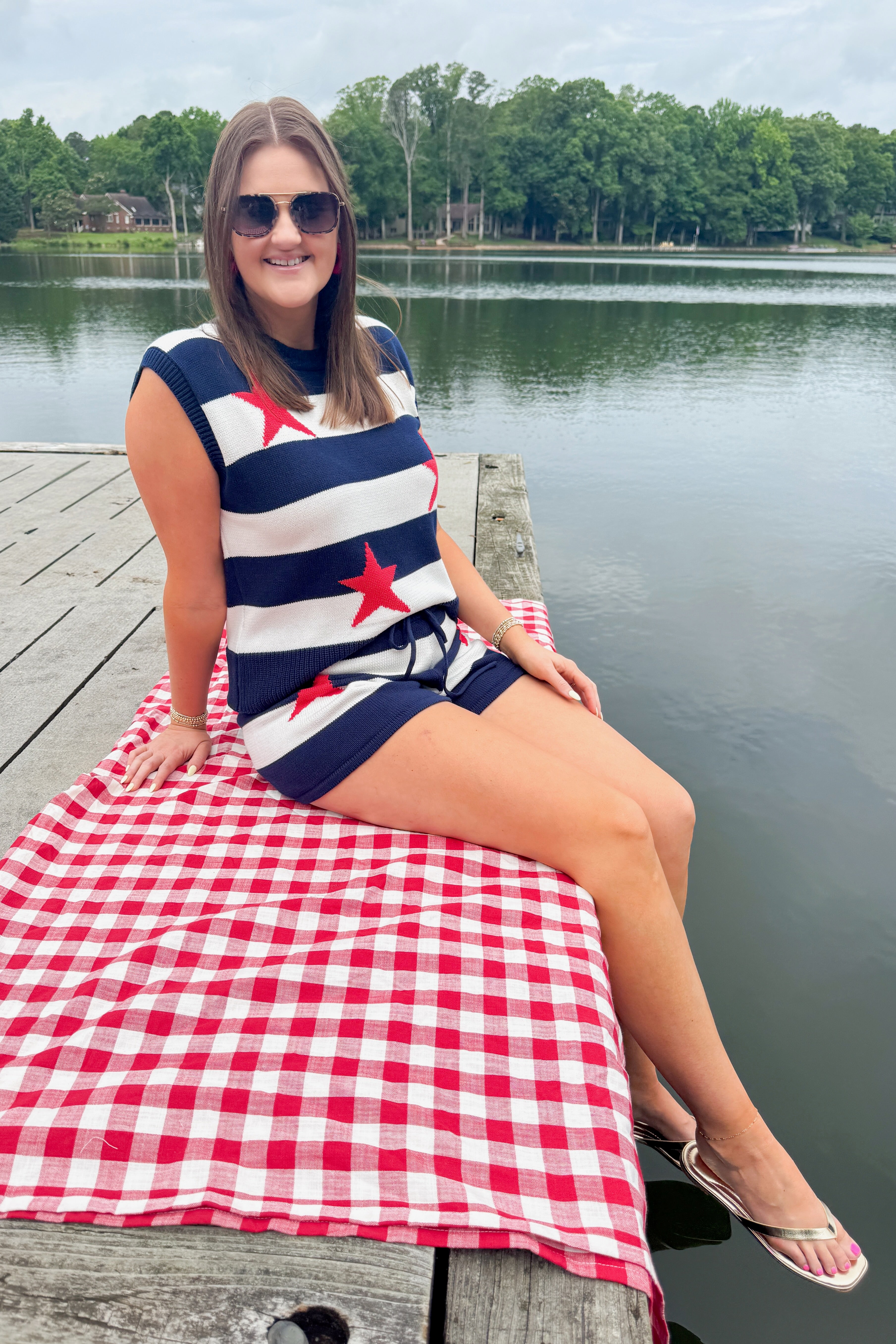 Front view of woman wearing Swagger Boutiqueβs Navy Striped Star Print Sleeveless Sweater with matching shorts outside at the lake.