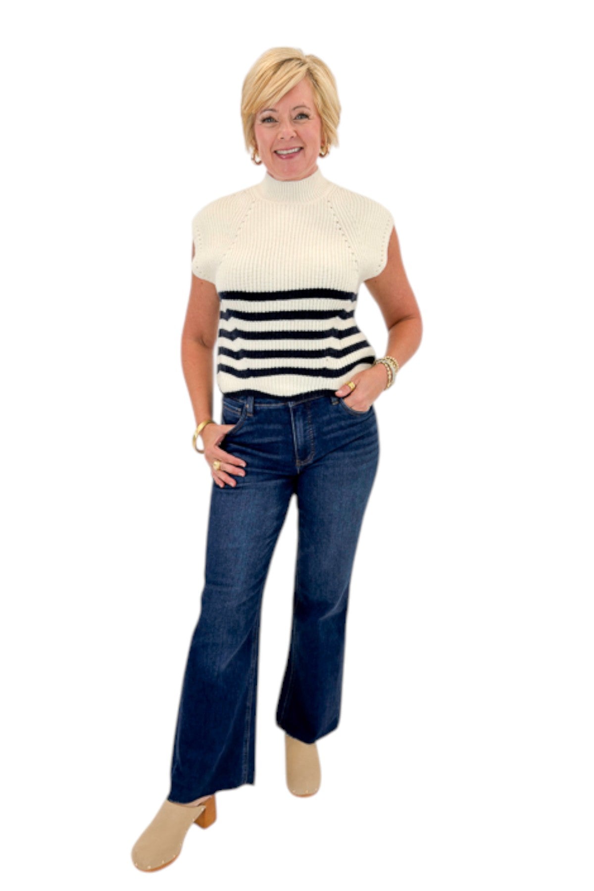 Front view of woman wearing Swagger Boutiqueโs Navy Striped Turtleneck Sleeveless Sweater with jeans against white studio background.