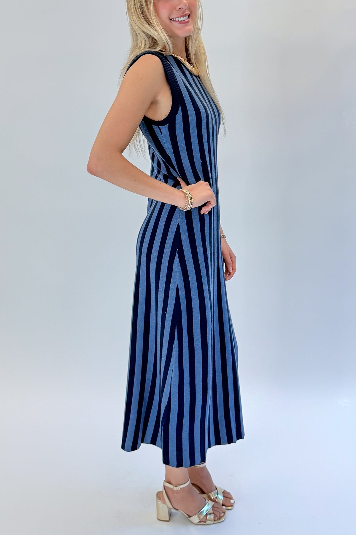 Side detail view of woman wearing Swagger Boutique’s Navy & Blue Striped Midi Dress with heels against white studio background.