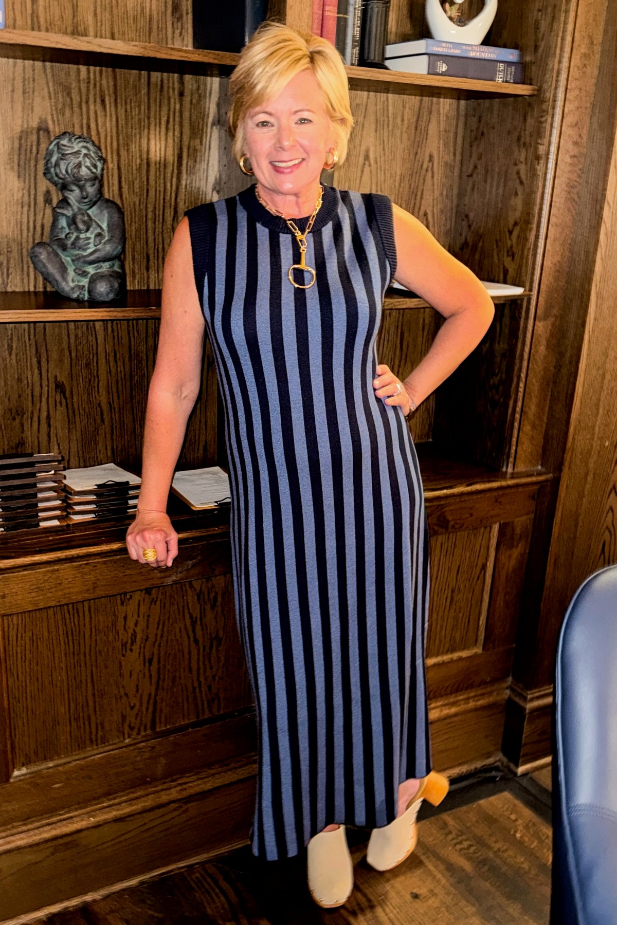 Front view of woman wearing Swagger Boutique’s Navy & Blue Striped Midi Dress with clogs at a library and den.