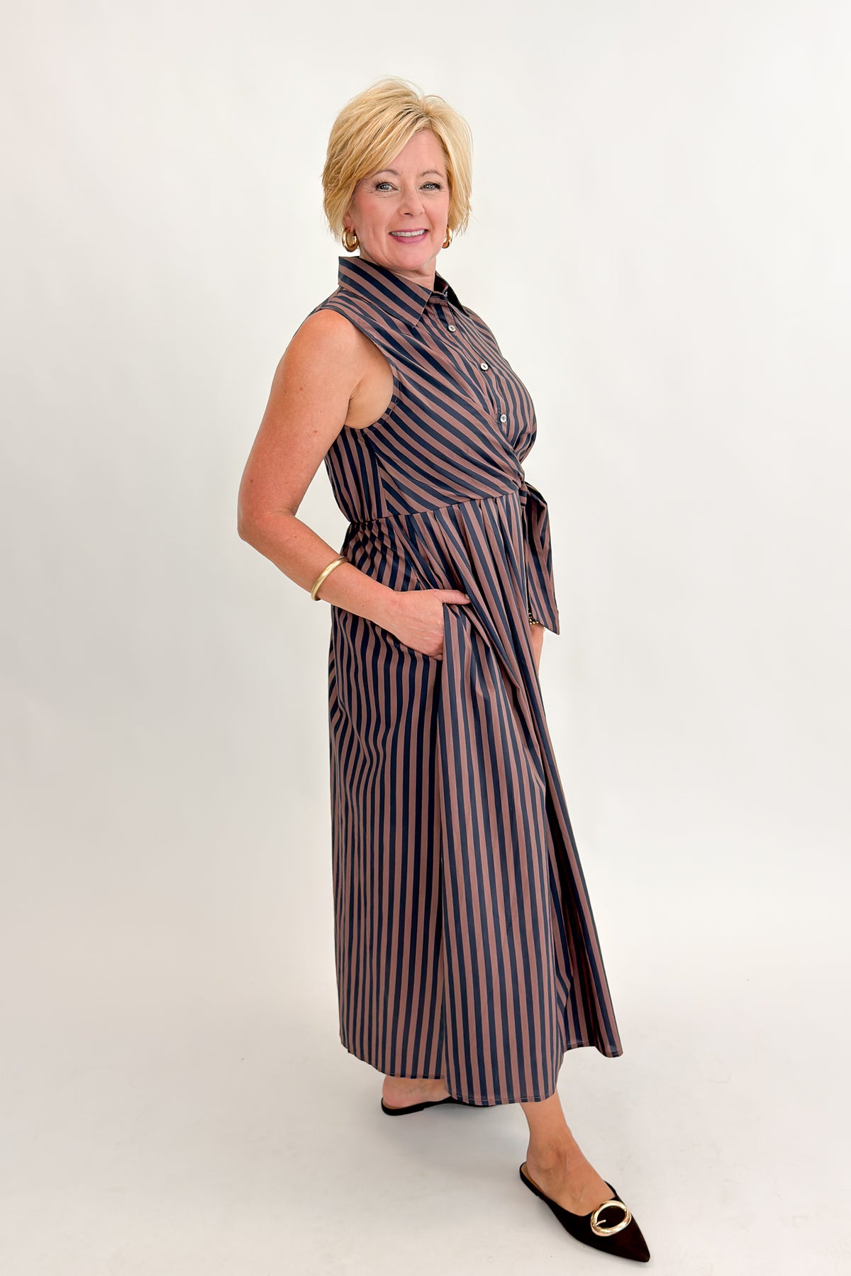 Side view of woman wearing Swagger Boutique’s Navy & Brown Striped Midi Dress With Tie by Entro against white studio background.