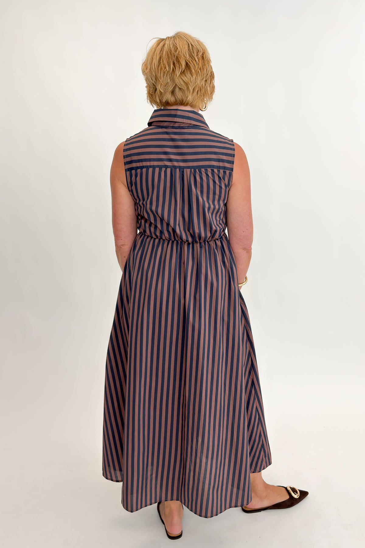 Back view of woman wearing Swagger Boutique’s Navy & Brown Striped Midi Dress With Tie by Entro against white studio background.