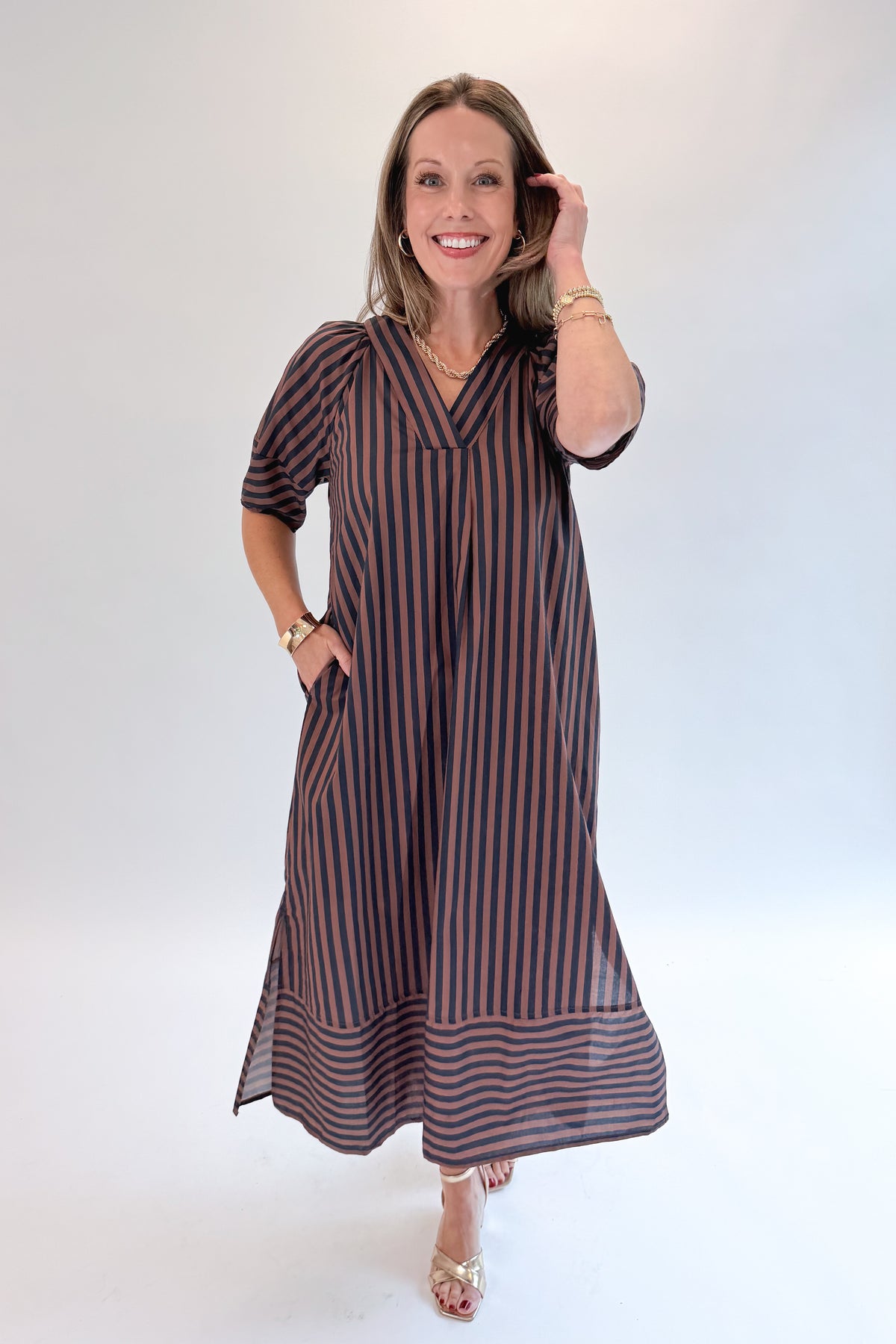 Front view of woman wearing Swagger Boutique’s Navy & Brown Striped Puff Sleeve Midi Dress by Entro with heels against white studio background.
