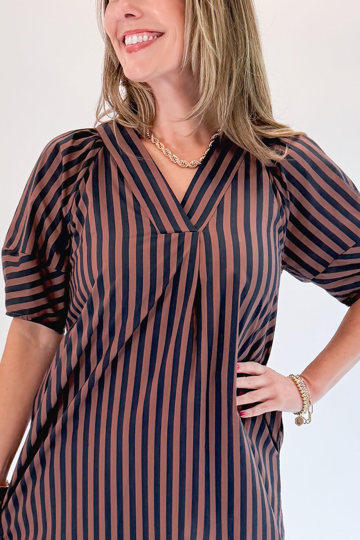 Front detail view of woman wearing Swagger Boutique’s Navy & Brown Striped Puff Sleeve Midi Dress by Entro with heels against white studio background.