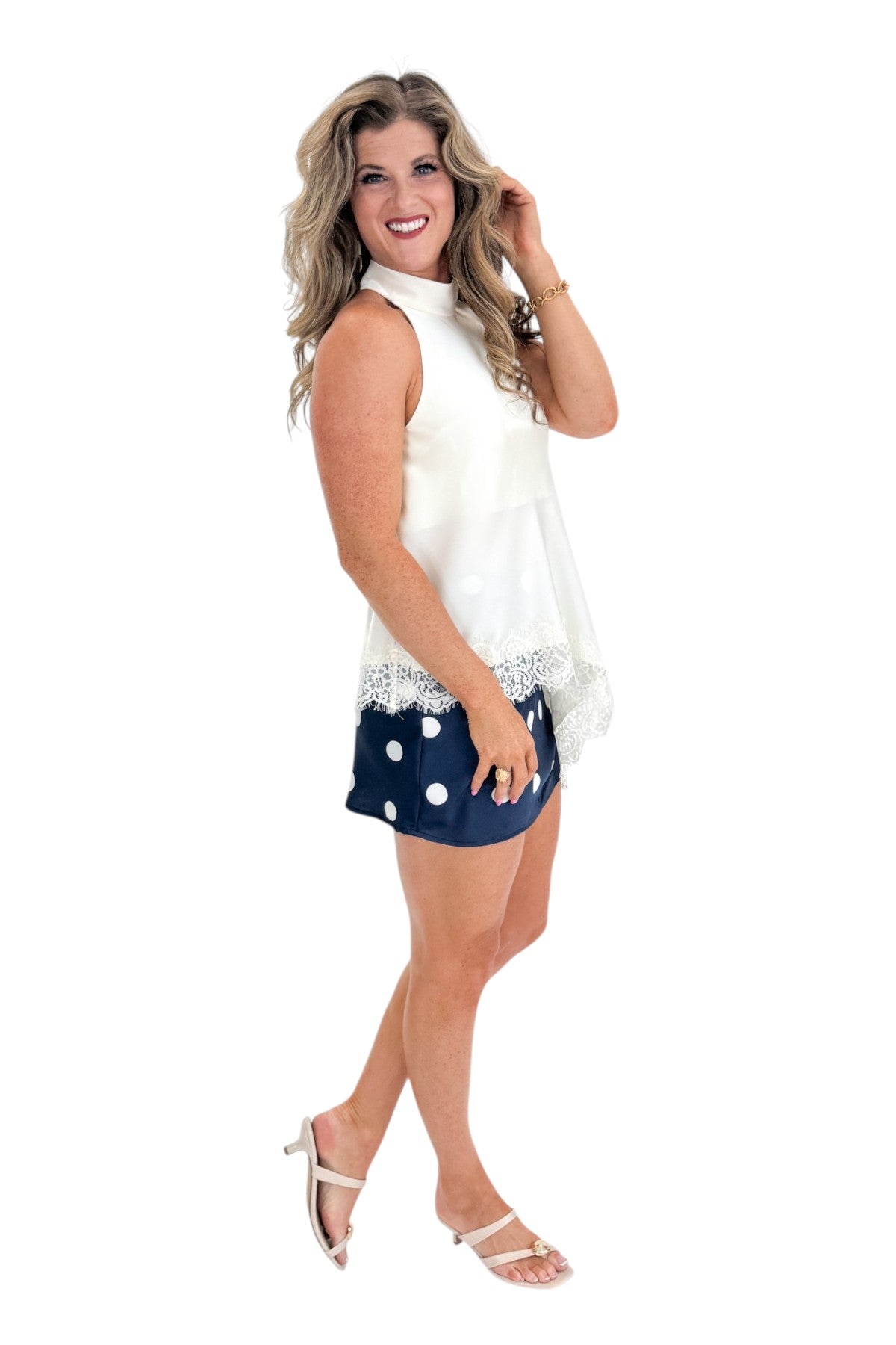 Side view of woman wearing Swagger Boutiqueās Navy & Cream Polka Dot Satin Mini Skirt with white top against white studio background.