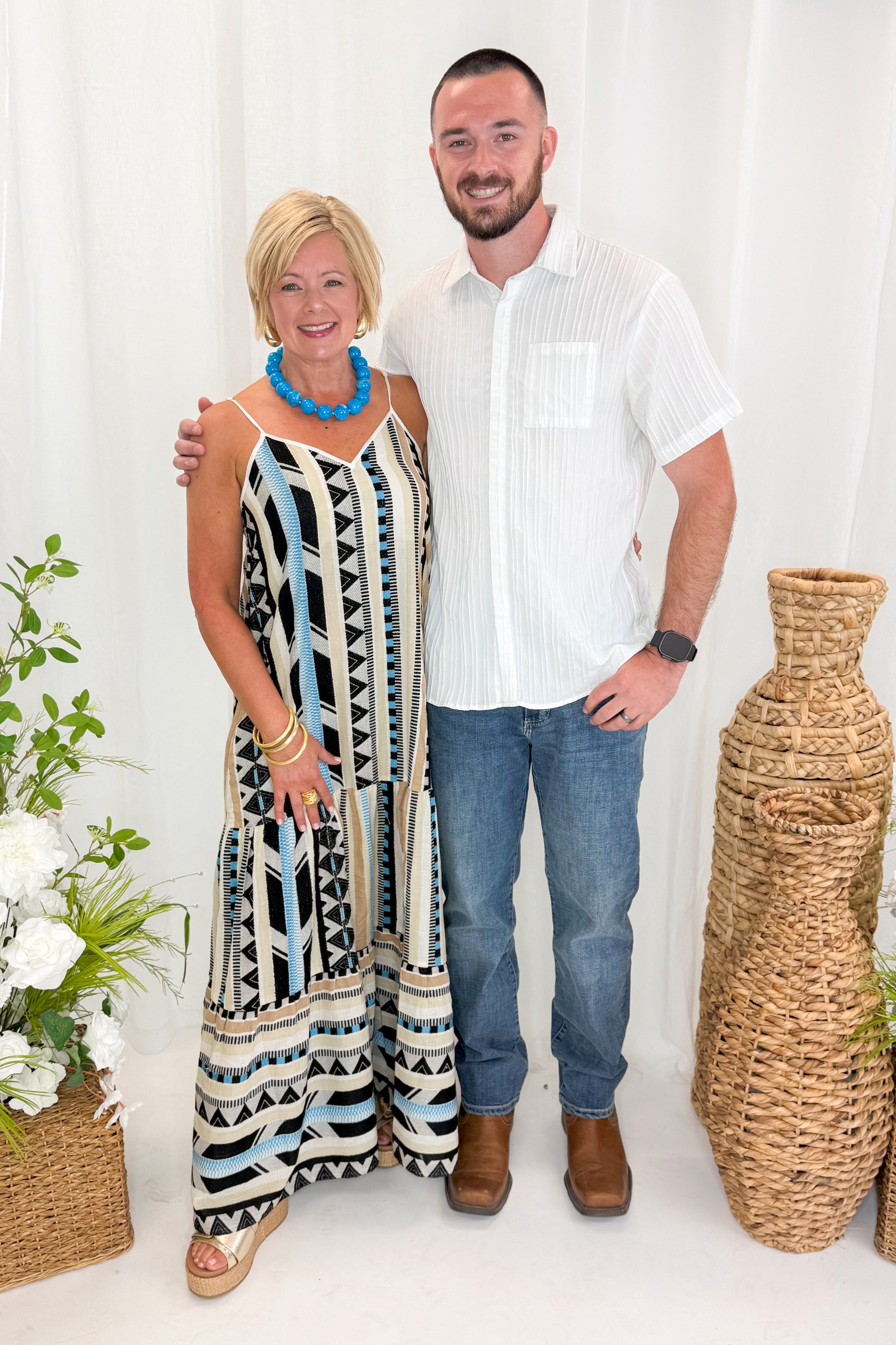 Front view of woman wearing Swagger Boutique’s Neutral Aztec Print Maxi Dress with sandals and son against decorative background.