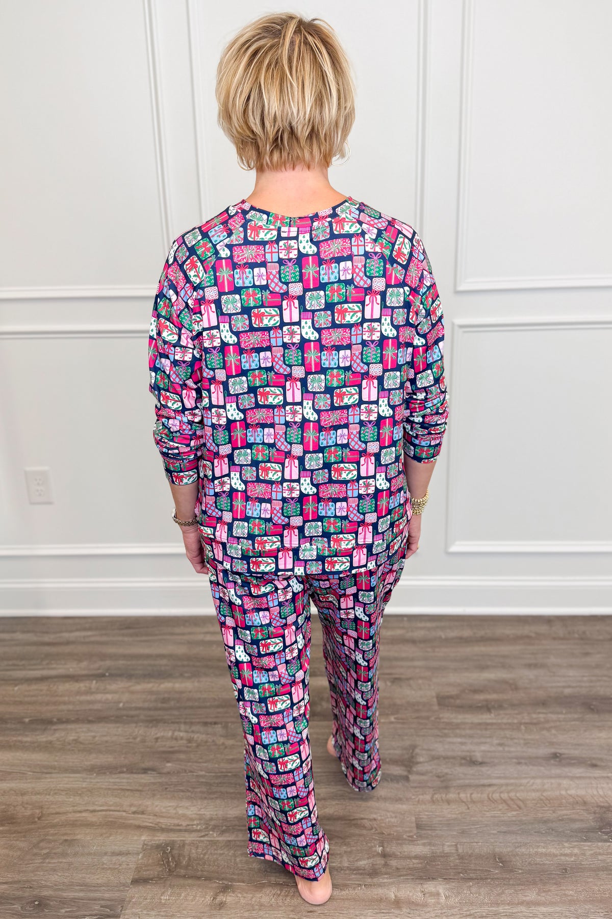 Back view of the No Peeking Navy Annie Pajama Set, showcasing the allover holiday gift box print with colorful presents, ribbons, and bows against a navy background. The long-sleeve pajama top features a comfortable, relaxed silhouette paired with matching full-length pants.