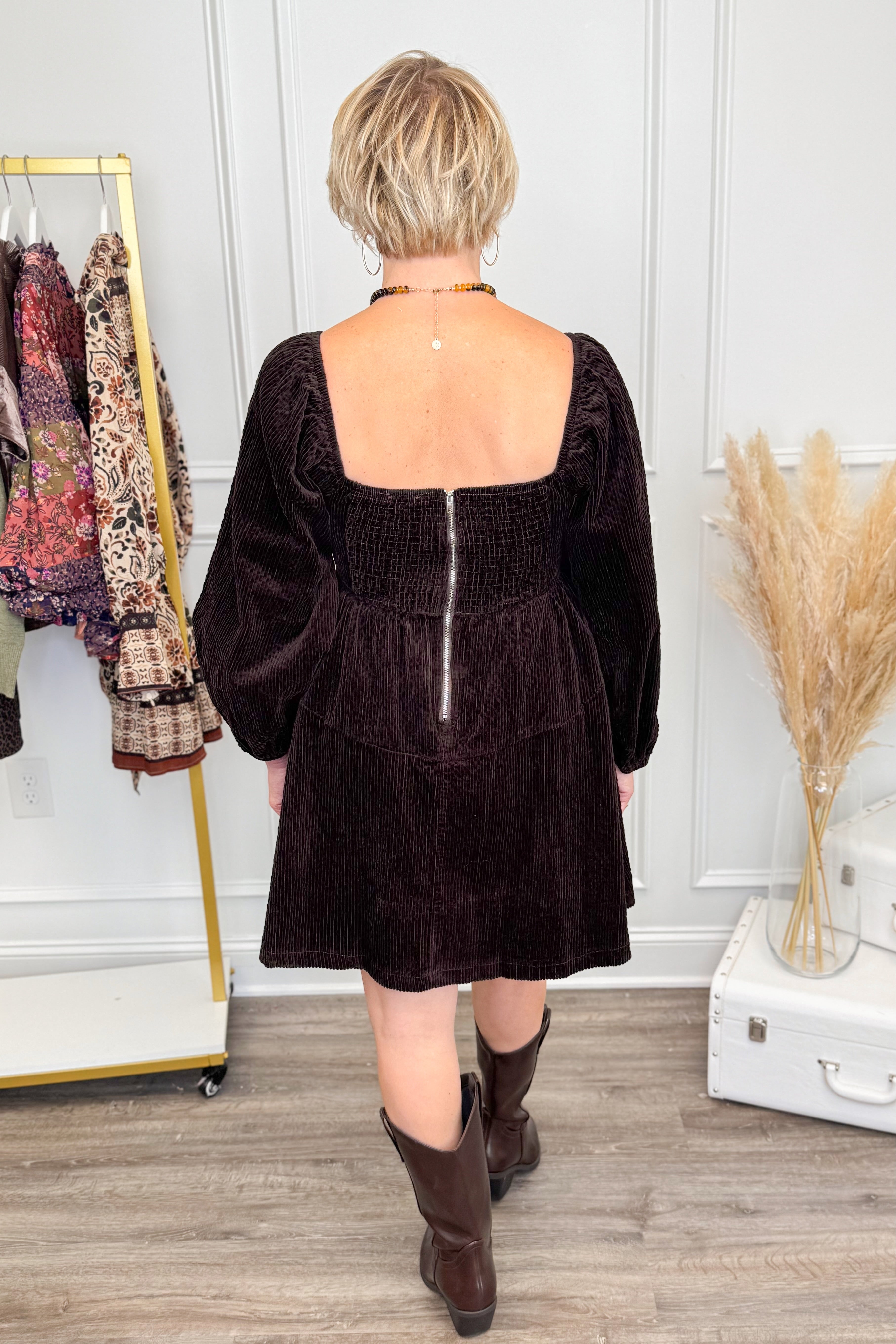 Back view of Woman wearing Brown Corduroy Puff Sleeve Dress and boots with decor in background.