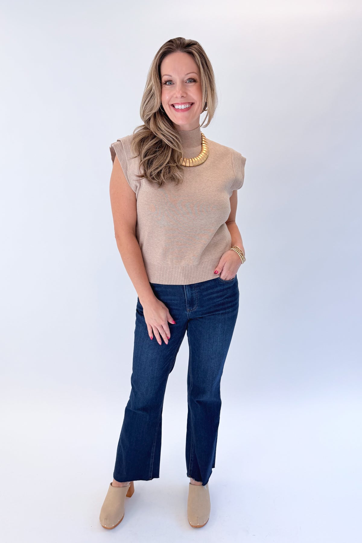 Front view of woman wearing Swagger Boutique’s Oatmeal Mock Neck Sleeveless Sweater by Entro with jeans against white studio background.