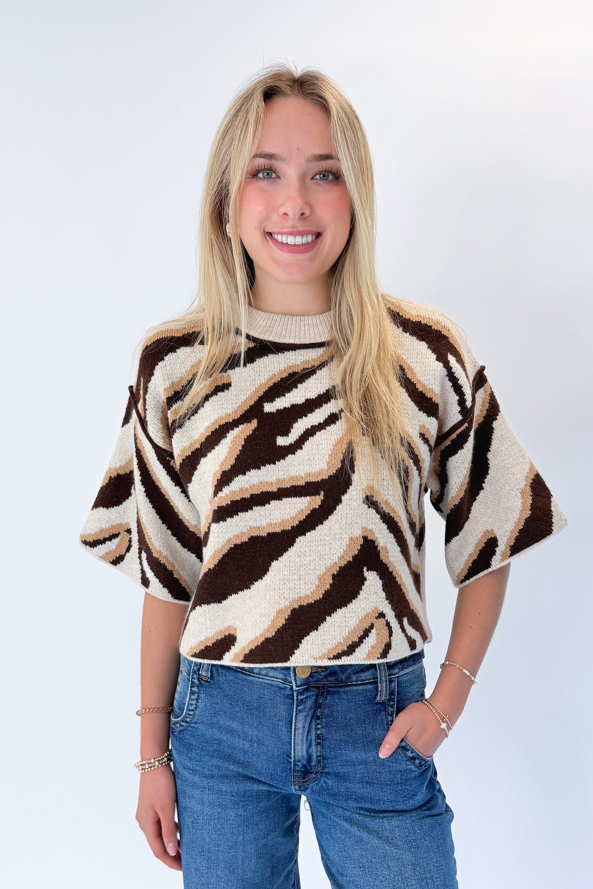 Front view of woman wearing Swagger Boutique’s Oatmeal & Brown Zebra Short Sleeve Sweater by Entro with jeans against white studio background.