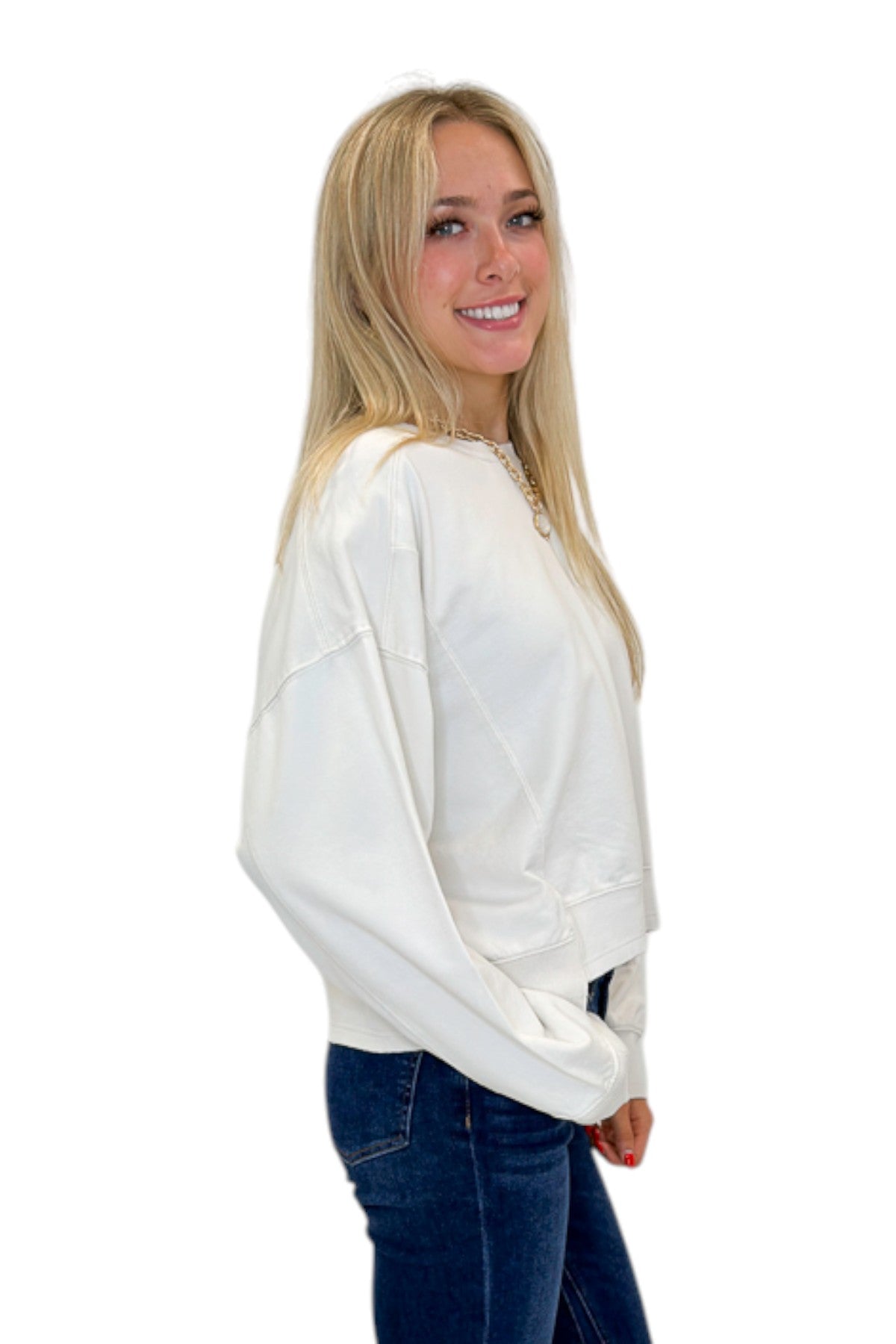Side view of woman wearing Swagger Boutiqueās Off White Ribbed Detail Sweatshirt with jeans against white studio background.