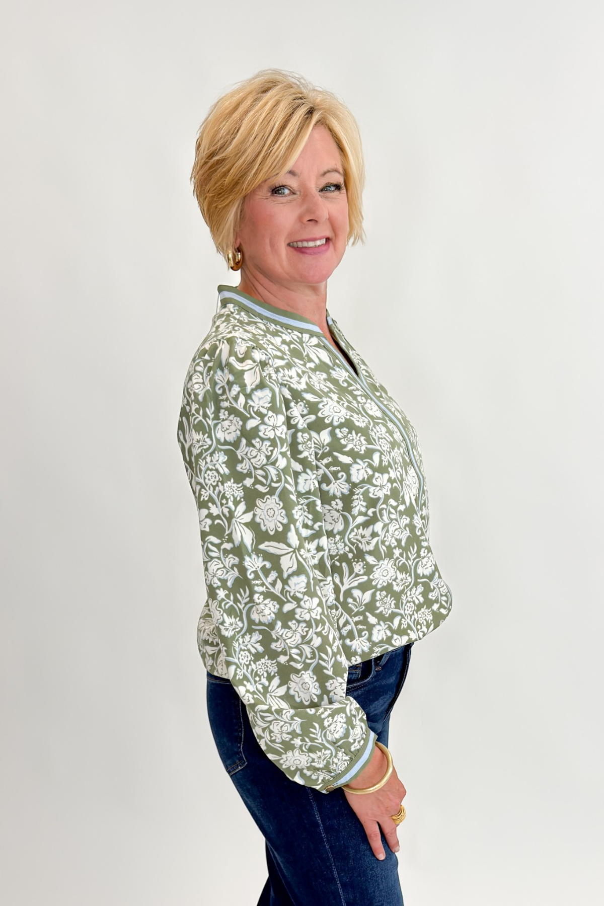 Side view of woman wearing Swagger Boutique’s Olive Floral V-Neck Top with jeans against white studio background.