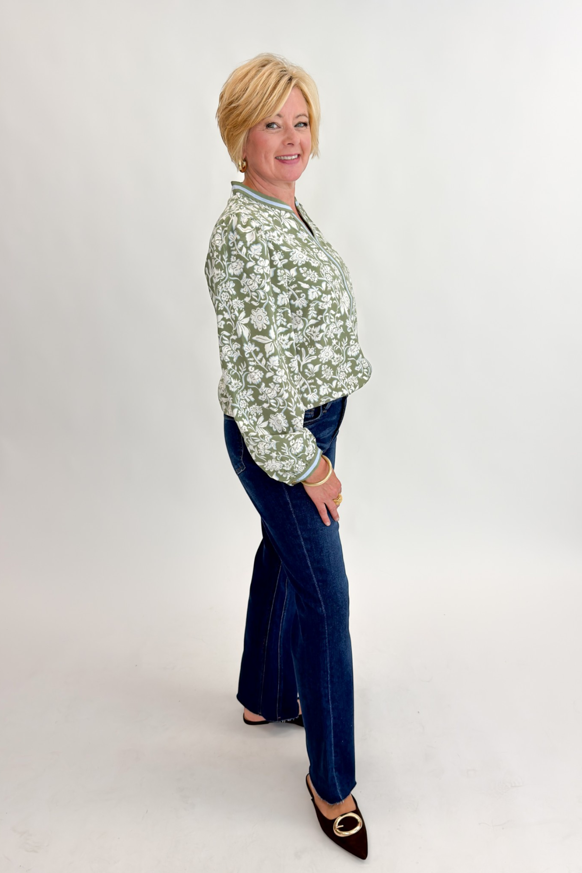 Side view of woman wearing Swagger Boutique’s Olive Floral V-Neck Top with jeans against white studio background.
