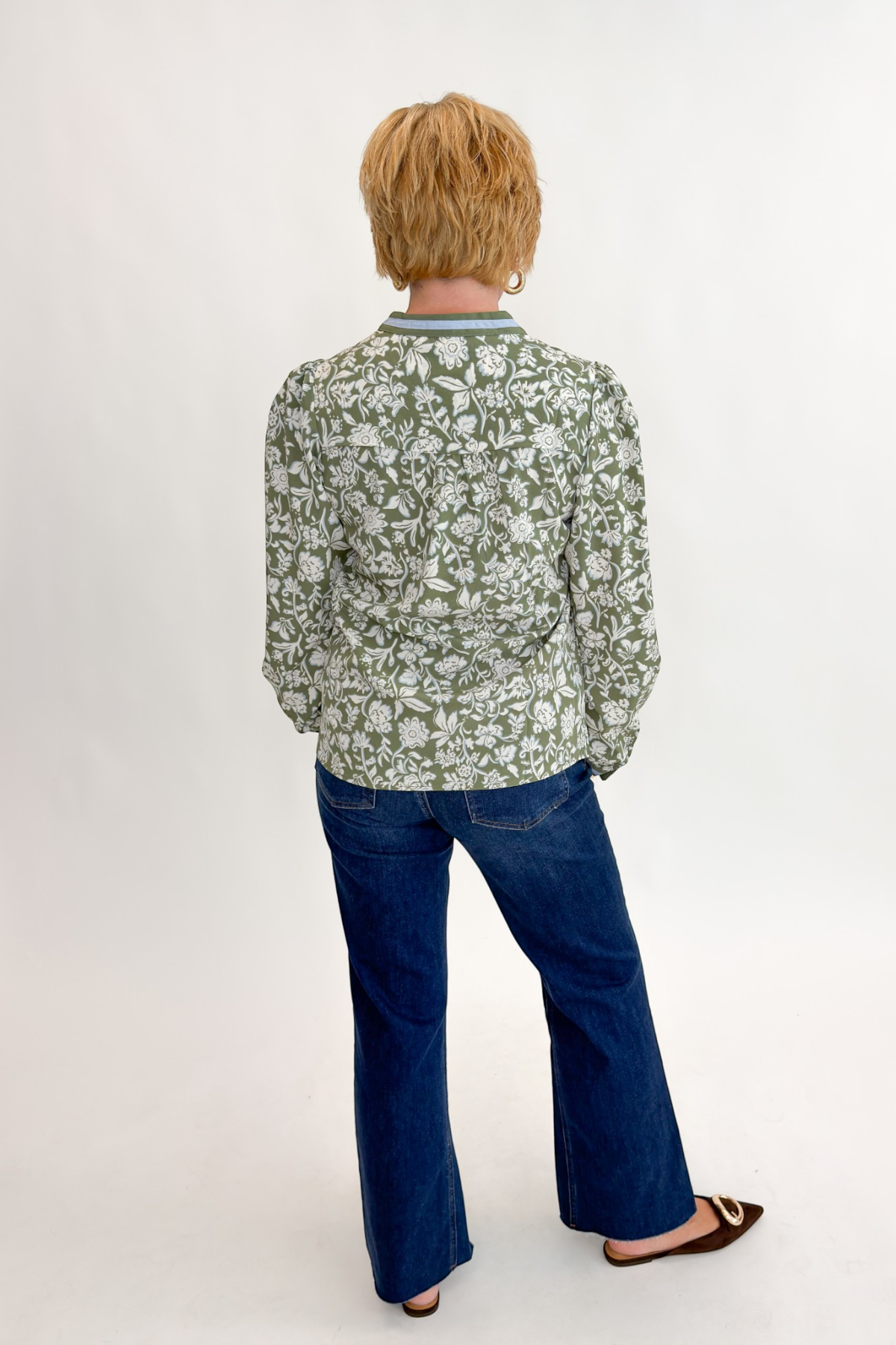 Back view of woman wearing Swagger Boutique’s Olive Floral V-Neck Top with jeans against white studio background.