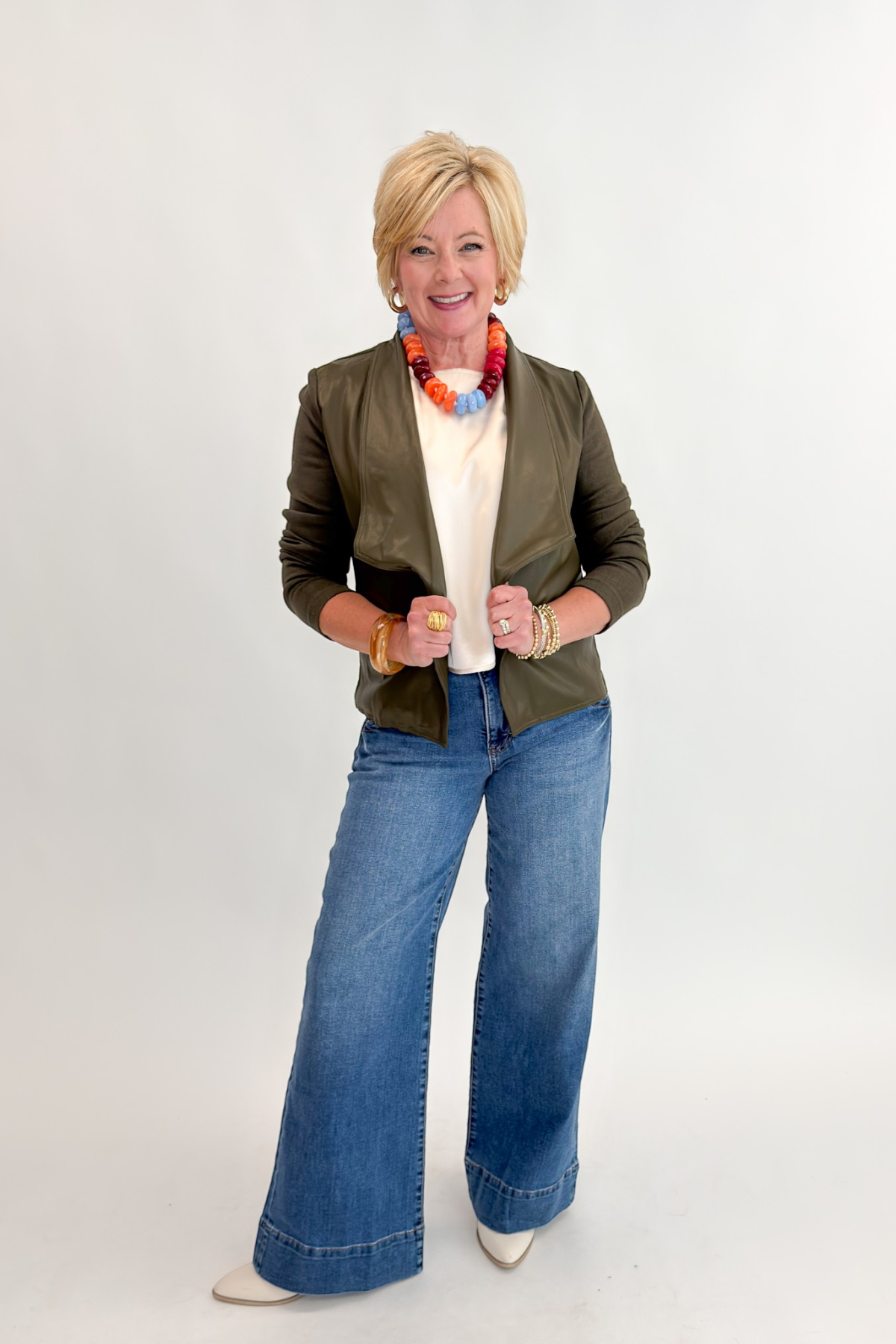 Front view of woman wearing Swagger Boutique’s Olive Knit & Faux Leather Draped Jacket with Maya Wide Leg Jeans In Medium Wash- Journey by Kut from the Kloth against white studio background.